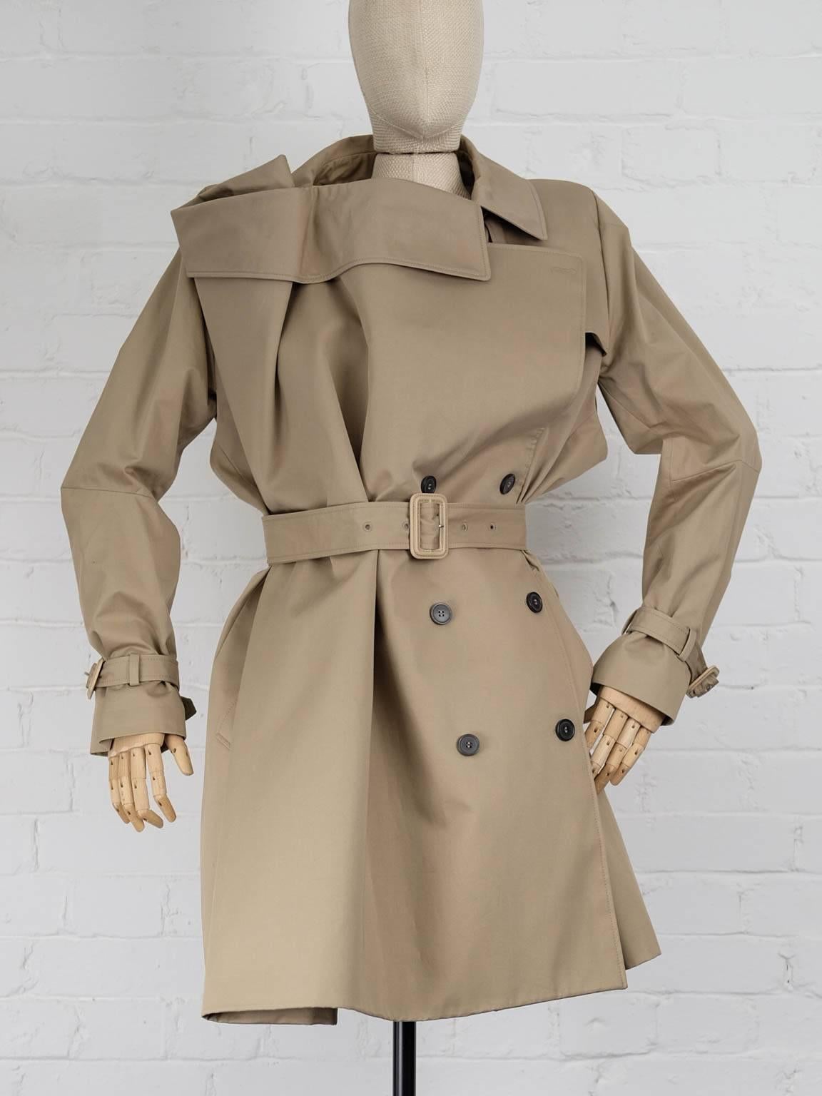 Tan cotton deconstucted trench coat featuring an asymmetric style, a double breasted front fastening, a belted waist, long sleeves, button cuffs, a rear central vent, a full lining, a long length, a side pocket and a structured storm flap.

Total