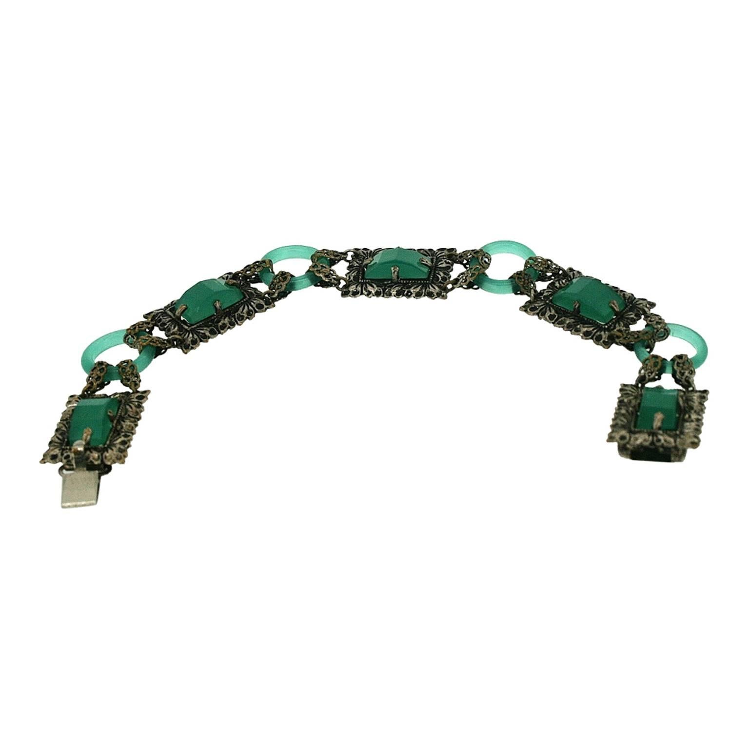 This bracelet dates from the 1920s and is unsigned. It features beautiful green glass panels. 
Condition Report:
Very Good - One small chip to the corner of one glass cabochon.  This is consistent with age and use and does not detract from the