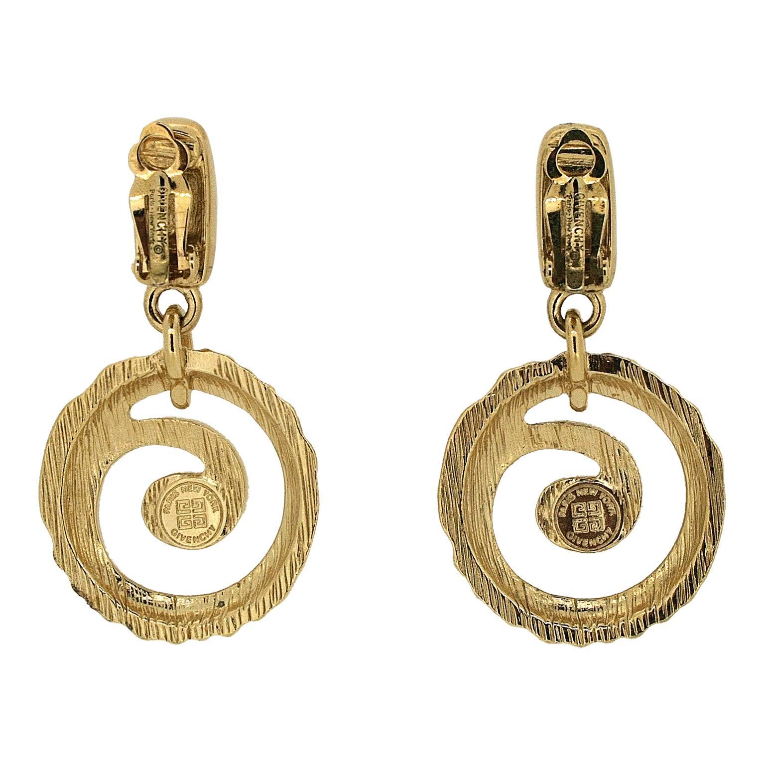 These glamorous drop earrings were made in the 1980s by Givenchy.
Condition Report:
Excellent 
The Details...
These shiny gold tone earrings feature a rectangular shape, suspended from which is a hammered metal circle with a swirling design cut out.