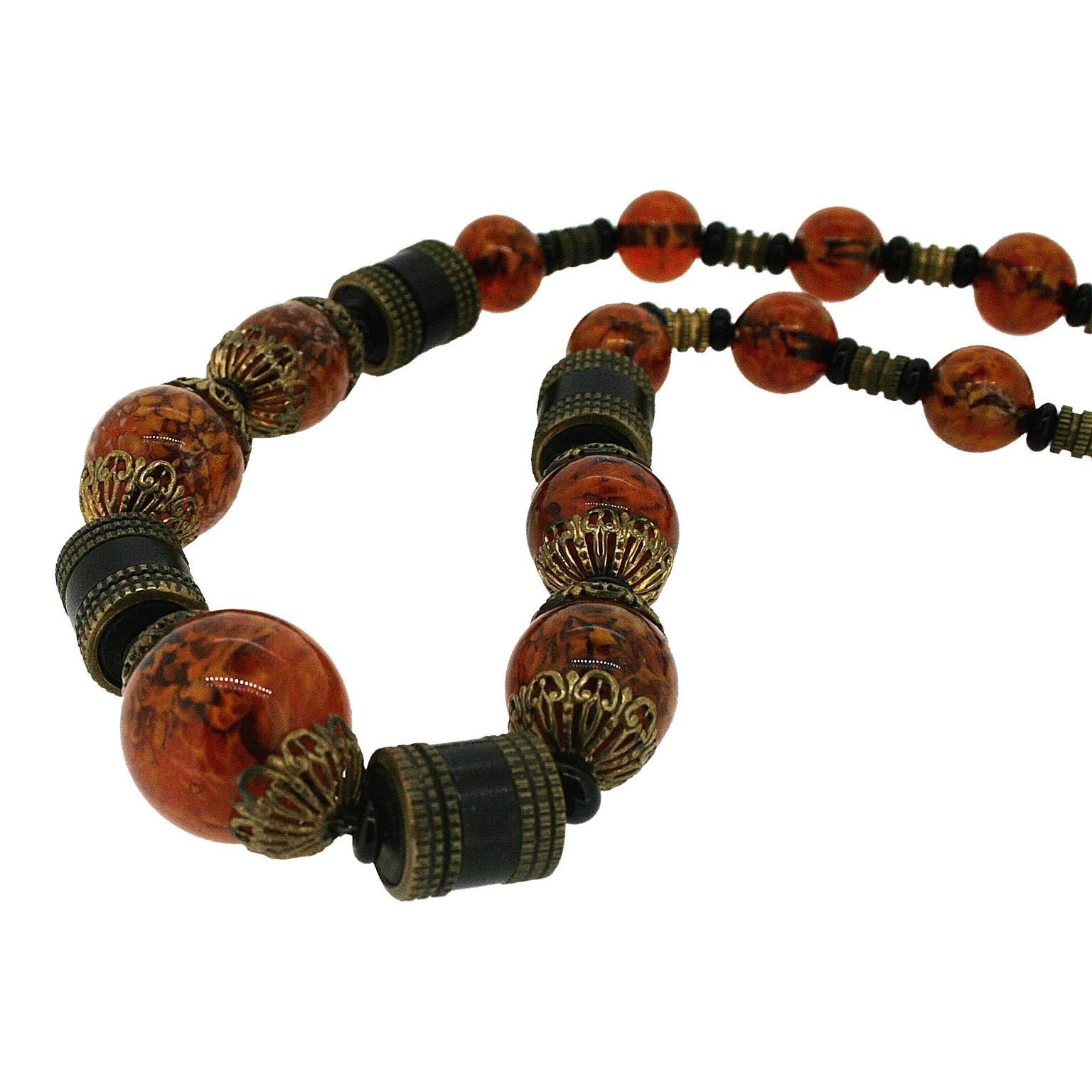 This beautiful necklace in a stylish amber hue dates from the 1930s. It was created in Czechoslovakia.
Condition Report:
Excellent
The Details...
This necklace features round marbelled amber glass beads, black rondelle shaped beads, brown wooden