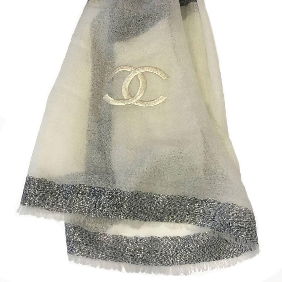 Beautiful CHANEL shawl with small fringes in ivory and anthracite silk and cashmere, dark gray border and silver thread. A large double C of pearly color is embroidered on the bottom of the stole.

Never worn. Chanel labeled.

Delivered in a Valois