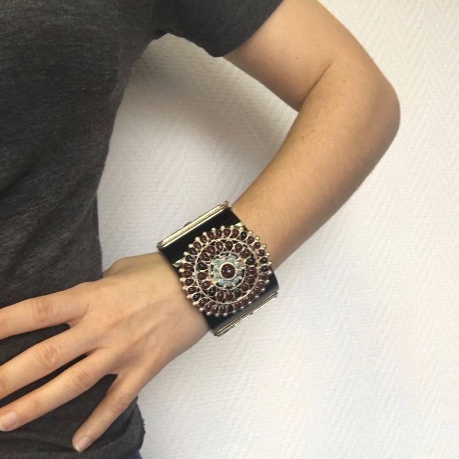 CHANEL cuff in black resin, gilded metal and molten glass. Superb piece adorned with molten glass garnet and turquoise in the center of the bracelet. A small golden CC in the front.

Push button closure. Chain of safety. Brand mark present on the