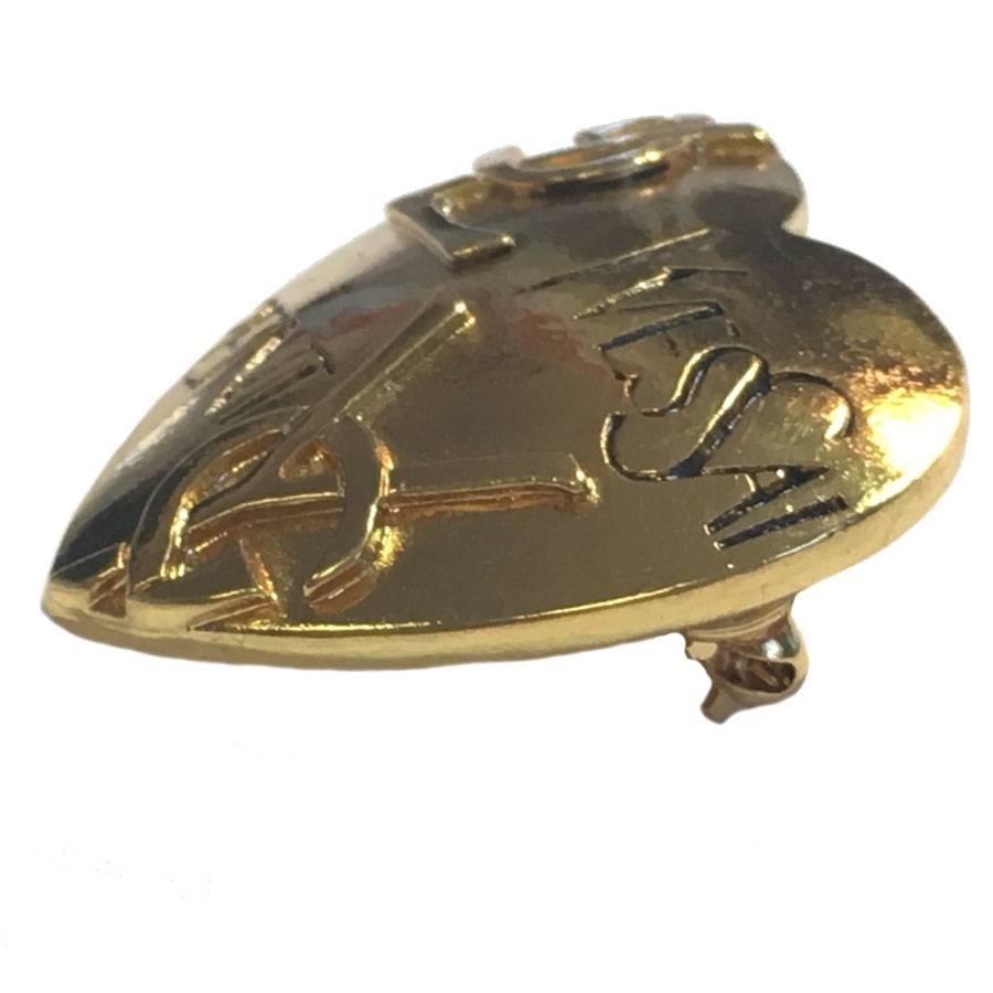 YVES SAINT LAURENT heart brooch in gilt metal. 

There is a hook in the back to wear it as a pendant.

Name and initials of the brand are engraved on the front of the heart.
