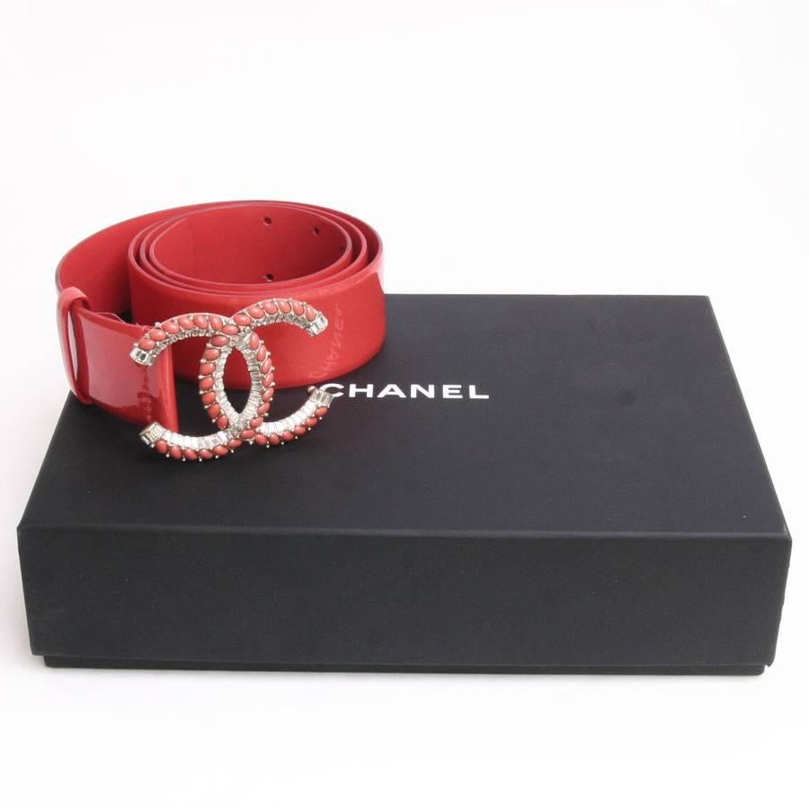 Beautiful Chanel waist belt in orange patent leather and buckle set with oval beads coral and shining emerald cut Swarovski.

The back of the jewelery is in gilt metal.

It will be delivered in its box Chanel