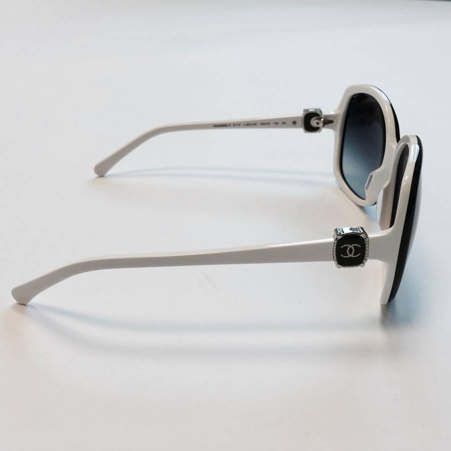 Very nice pair of sunglasses CHANEL. The frame is in white acetate and black glasses outline. Glasses are in a gray gradient. 

Dimensions: height of the lenses: 5 cm - frame width: 13,5 cm - length of the branches: 14 cm

Delivered in its pouch,