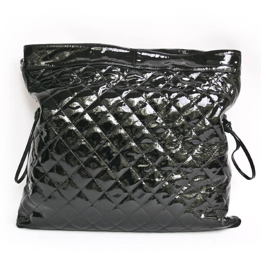 Chanel messenger bag in black patent leather (Big size). One part is smooth and the other part is quilted. Snap closure. The hardware is in silver metal. The interior is in black canvas with 3 pockets including one zipped. 
At the front you will