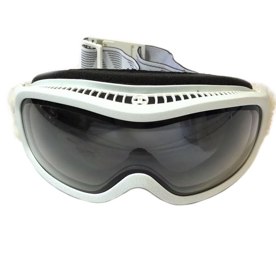 To be trendy on the slopes! CHANEL ski mask. White frame with crackle effect. Elasticated strap on the sides, CHANEL inscription in white. Clasp clip in white plastic with a CC on it. Glasses with a darker shade. 

Dimensions:
mask length: 21 cm -