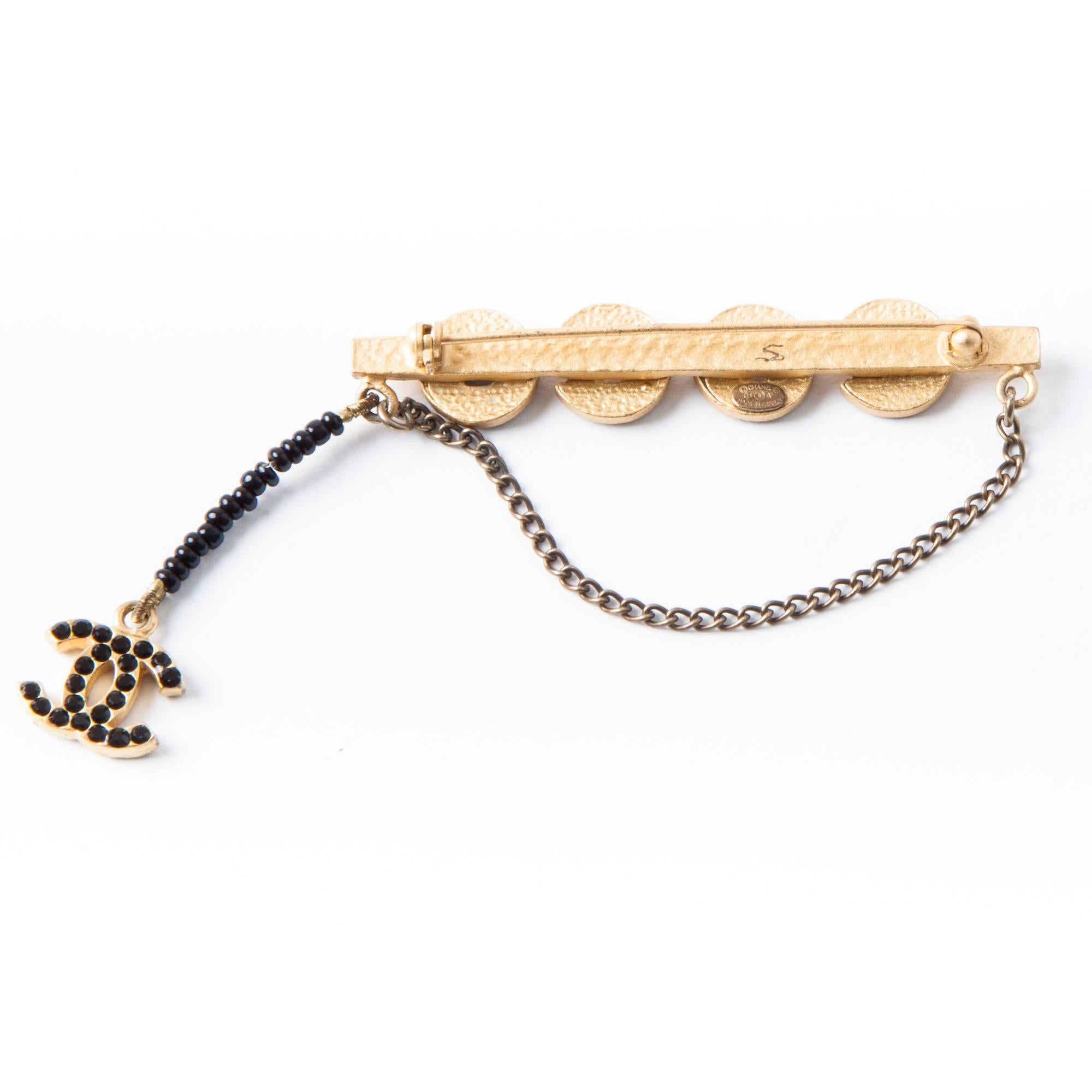 Beautiful Chanel brooch 'COCO' in matte gold color metal and black rhinestones. A small chain is at one end, made of black pearls and a CC set with small black rhinestones.

Fall / Winter 2001 collection

Dimensions: length: 5.9 cm, width of the