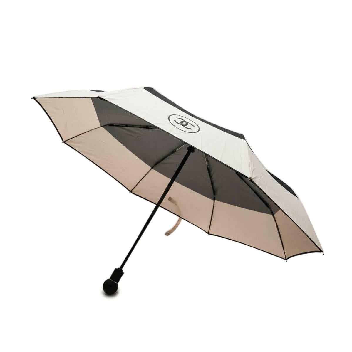 Chanel umbrella with 'CC' logo beige and black. Sold out at Chanel. A pressure on the handle of the umbrella allows to open it automatically.

New condition. Measures: 32 cm long. 

Worn on the shoulder or crossover in its cover by a silver