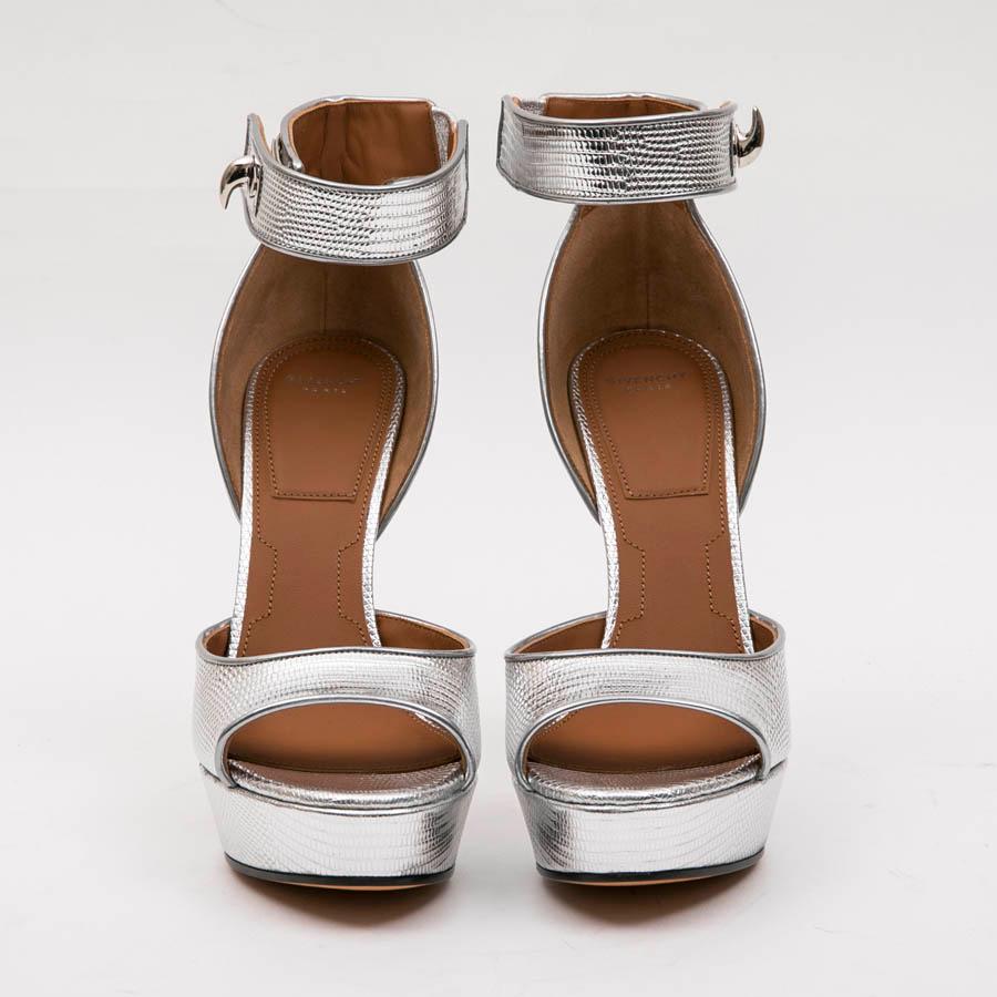 Givenchy's Shark Lock high heels sandals owe their name to the rotating clasp that characterizes a variety of home accessories. 

Their high-gloss silver leather has been embossed like a lizard skin for a textured finish. 

They are closed at the