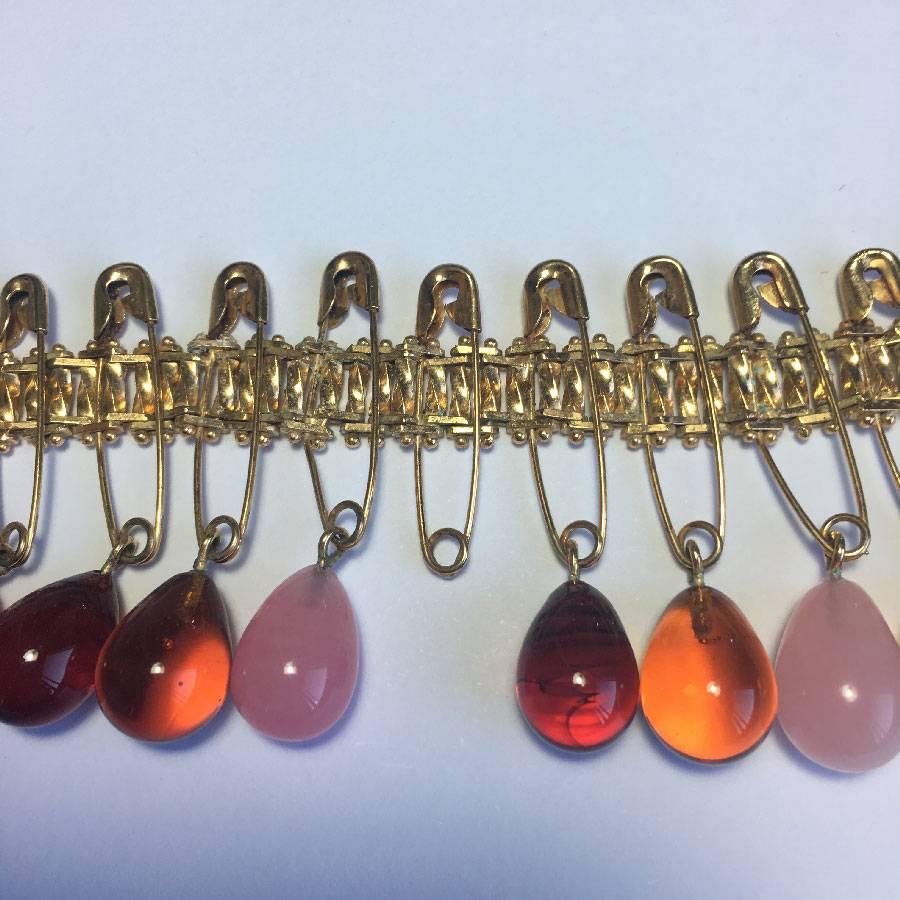 DIOR bracelet in gilded metal and oval beads in light and dark amber and pink molten glass attached by safety pins. 

In good condition. An oval pearl is missing in the middle

Dimensions: shortest length 16.5, longest 22.5 cm, width 4.5 cm.

Will