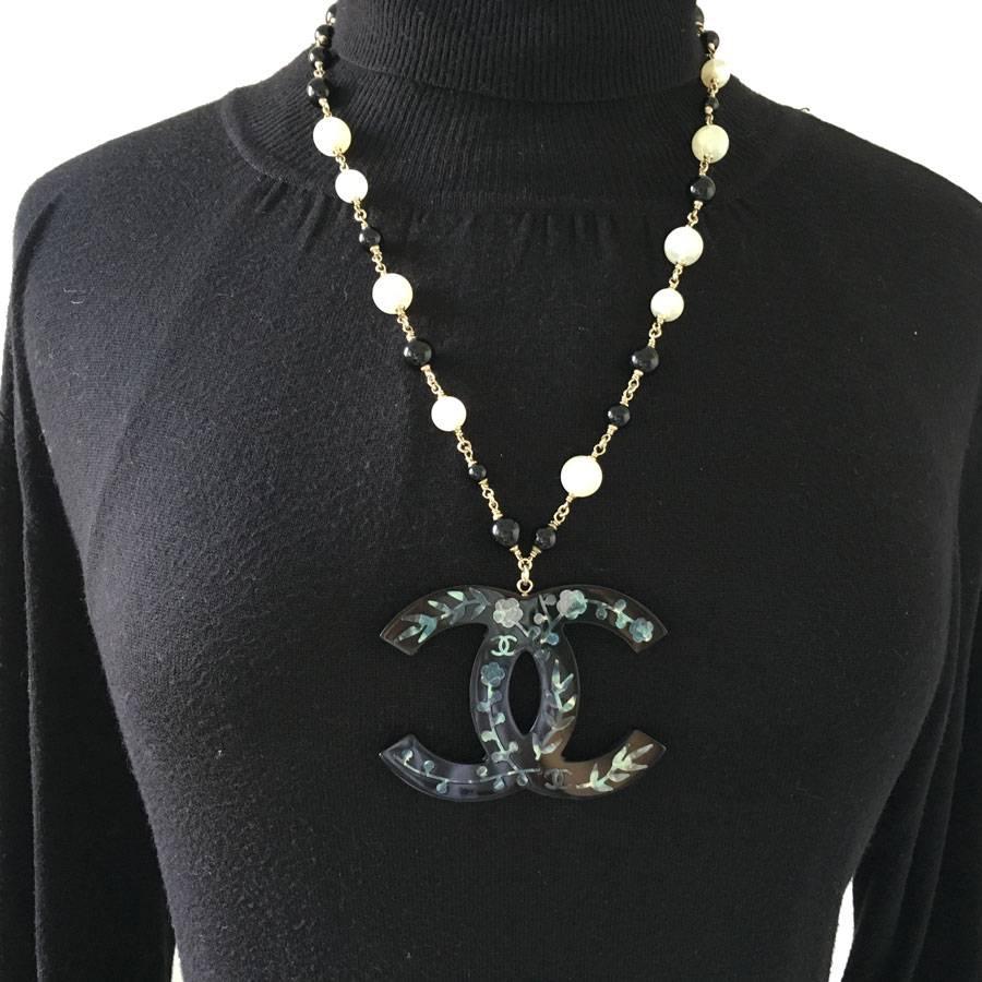 Very beautiful necklace Chanel CC with gilded metal chain, black and pearly pearls, pendant : double C in black resin encrusted with camellias and CC in mother-of-pearl.

In very good condition. The resin is slightly scratched on the back due to