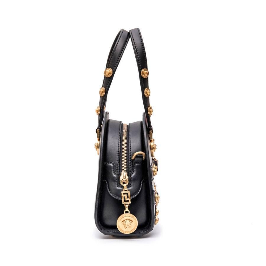 VERSACE 'Tribute' bowling bag in black soft calfskin leather. 

Revisiting a classic of the House, this piece is a tribute to Gianni Versace. 

Medusa medallions and gilded jewelery. Zip closure on the top. 

The interior is lined in leather.