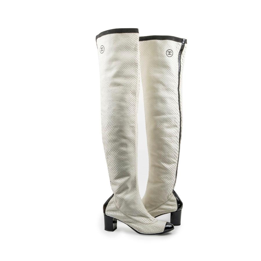 Chanel thigh boots in white python. They are lined in white leather. Black patent leather tip. Black leather band at the back of the shoe. Acronym 'CC' stitching at the top of the boot.
The heel is covered with black patent leather. Outsole and