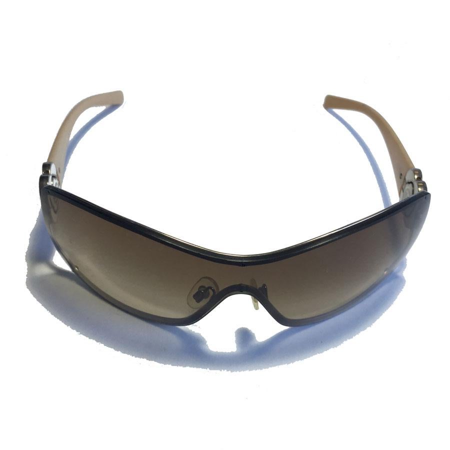 Les lunettes de soleil masque CHANEL sont composées de branches en métal et en plastique beige ornées d'un camélia en métal ivoire.

Indiquer correct. Quelques rayures sur les verres.

Dimensions : largeur : 14 cm - hauteur des verres : 5 cm -