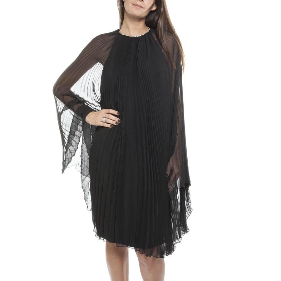 Sublime AZZARO evening dress in black silk, backless under a pleated black chiffon cape that leaves the neck.

A swarovski baguette crystal edging around the neck and on the décolleté in the back.

It closes with a staple behind the neck and a