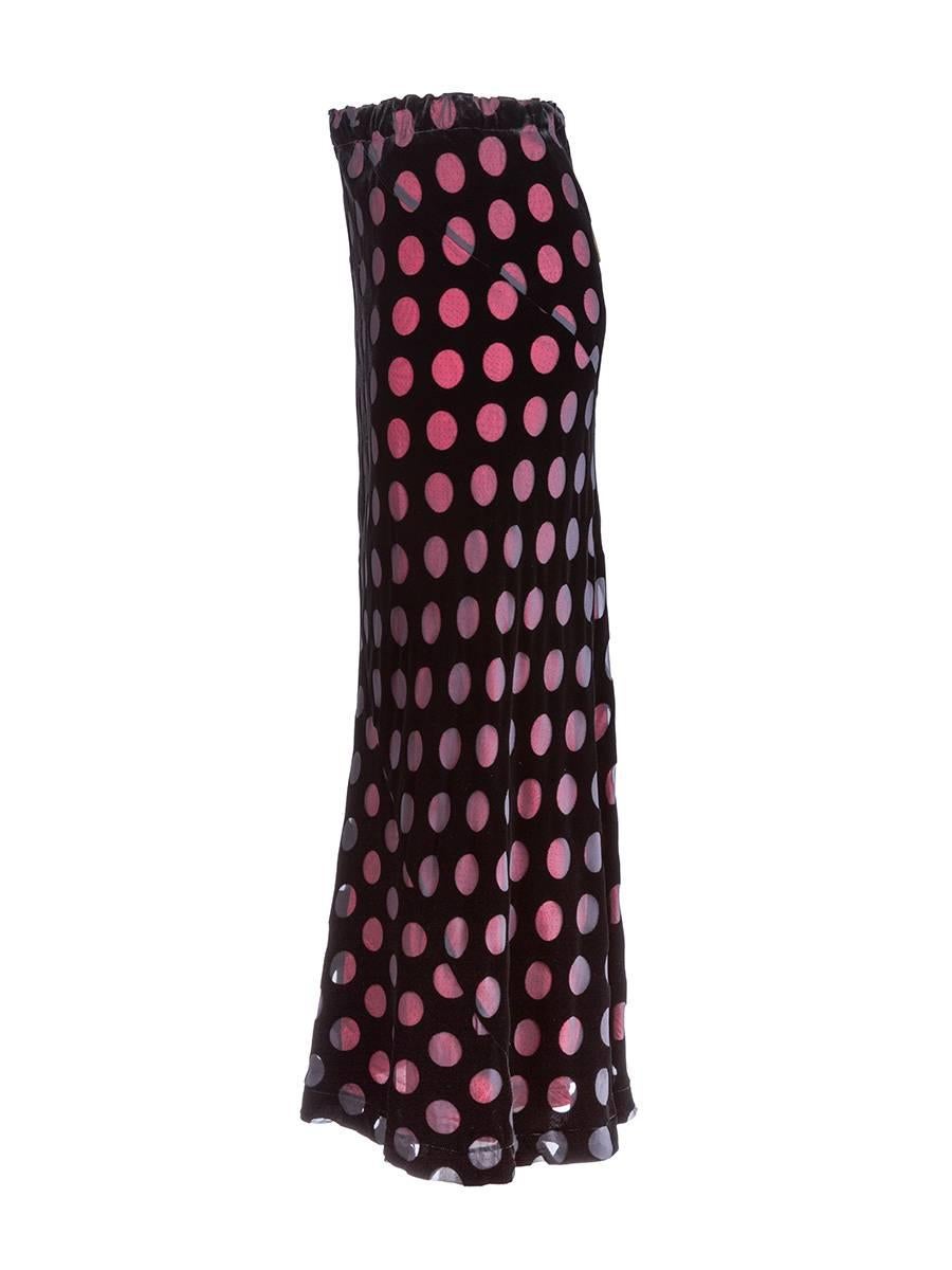 Vintage Comme des Garçons black velvet bias cut maxi skirt with polka-dot cutouts exposing a bright pink lining and an elastic waist.