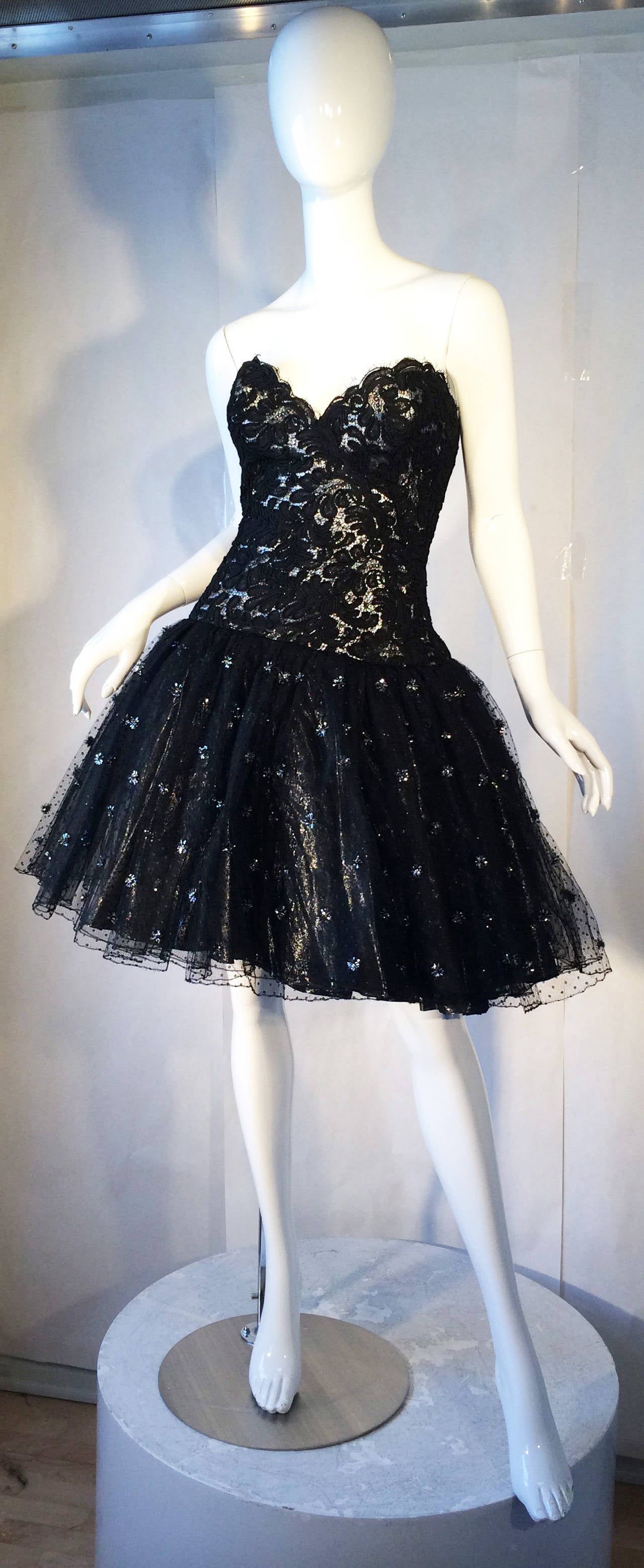 A fine and rare vintage Bob Mackie cocktail dress. Original custom order couture item features a fine black lace over a silver metallic bodice and multiple layers crinoline lace skirt with silver lurex details. Item fully silk lined with a boned