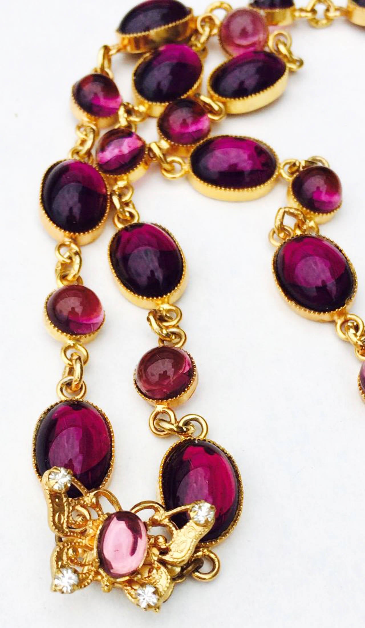 A fine and rare vintage William de Lillo pendant 'jeweled' pendant necklace. Signed gilt metal chain linked item suspends a matching 'jeweled' pendant. Swarovski crystals and both purple/pink glass cabochons set within gilt butterfly filigrees and