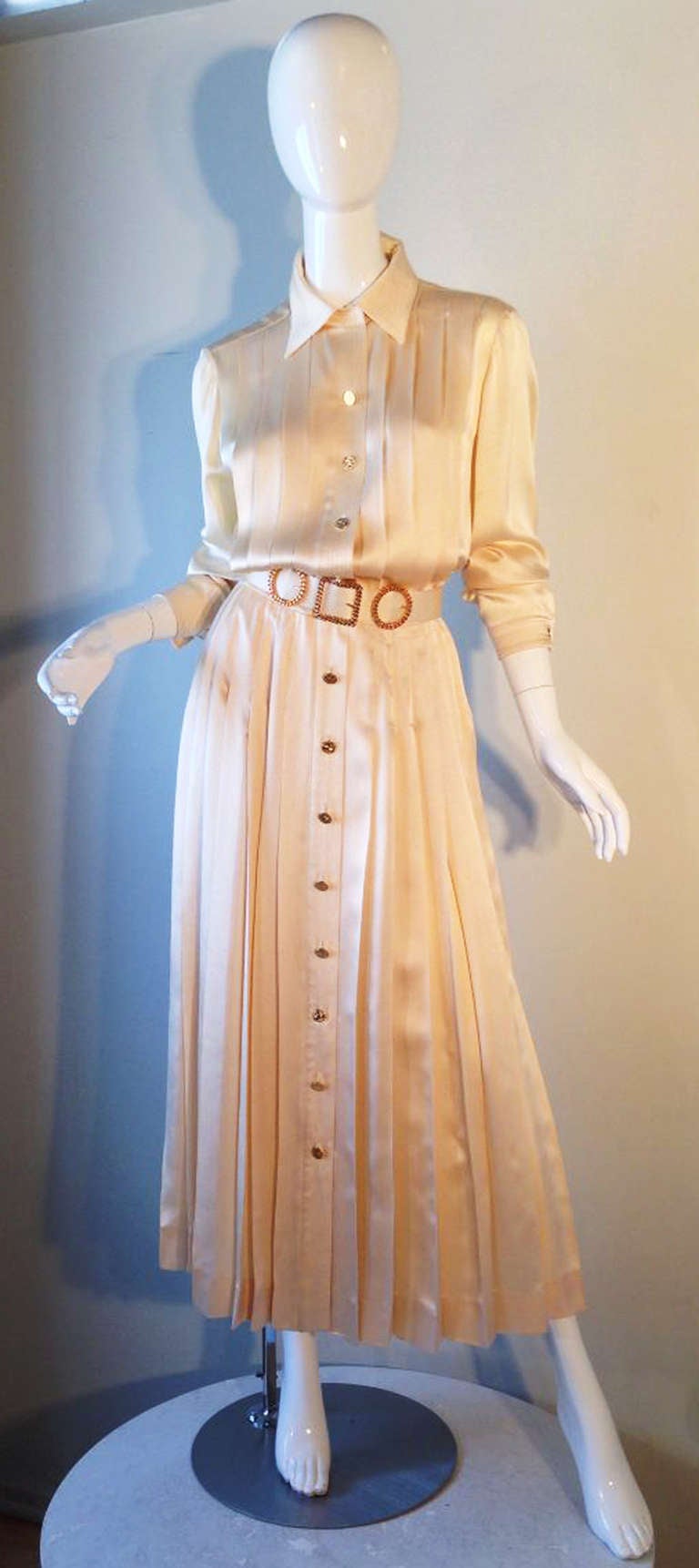 A fine and rare vintage Chanel dress and matching belt. Ivory silk charmeuse fabric dress features nipped waist, pleated bodice and tea length pleated skirt. Gilt signature button front with channel pleated collar and cuffs. Rare original matching