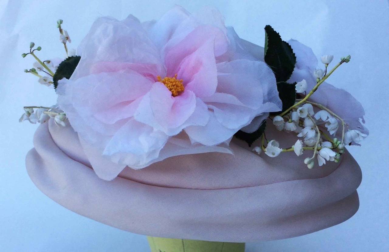 A fine and rare vintage Christian Dior haute couture hat. Charming pink silk spring theme item trimmed with hand constructed pink petaled blooms and sculpted lily of the valleys sprigs. Excellent and intact.