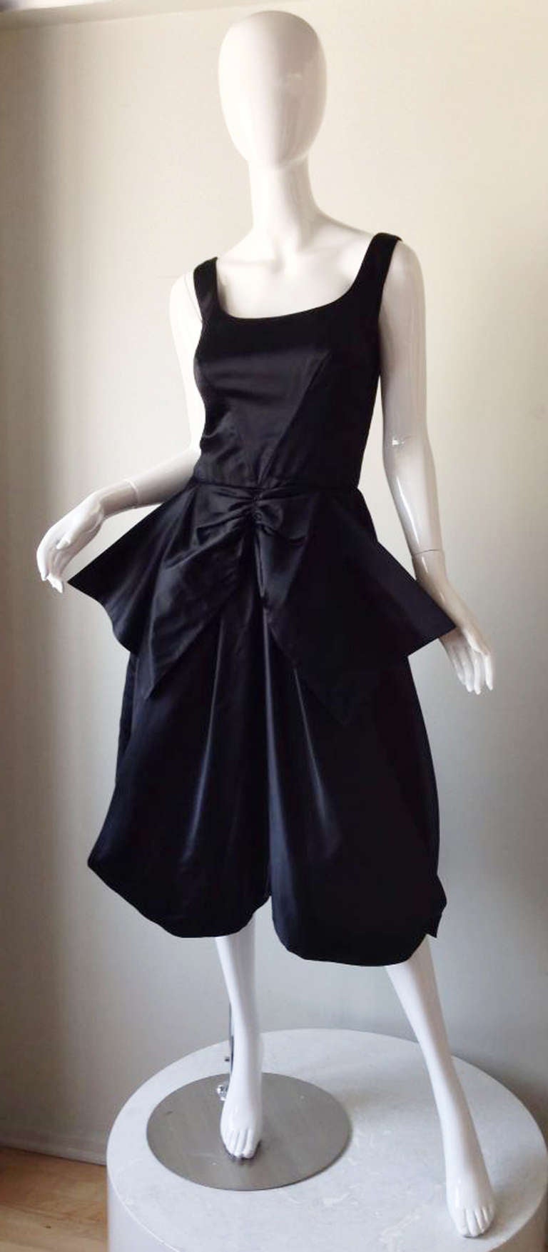 A fine and rare vintage Mr. Blackwell cocktail dress. Ink black silk satin item features full draped skirt and huge matching fabric bow center waist. Item fully lined and zips up back. Pristine.