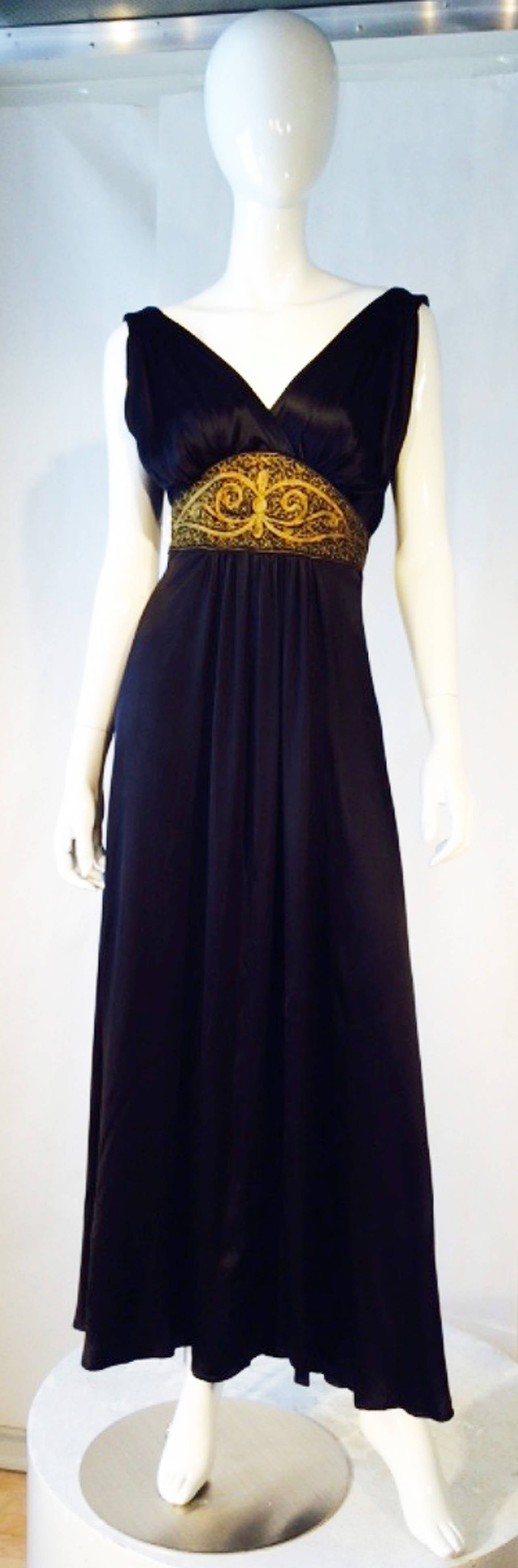 A fine silk gown with a embroidered waistband. Unlabeled jet black silk satin item features a hand embroidered waistband in a metallic gold wire. Bias cut item additionally pleated center front and shoulders. Gown buttons up back with a full sweep.