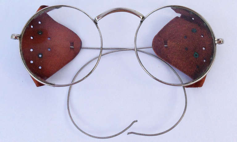 A fine and rare vintage pair motorcycle safety glasses. Nickel plated flex frames feature original optical glass lenses and vented leather visors. Pristine, appears unworn.