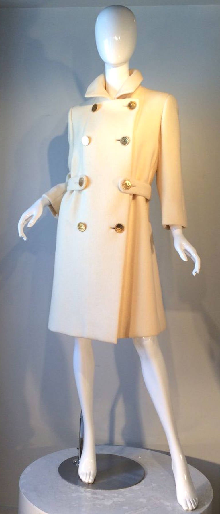 A fine Norman Norell coat. Fine ivory wool item features precision seams, double breasted front, half belt, large gilt metal buttons and fully silk lined. Pristine appears unworn.