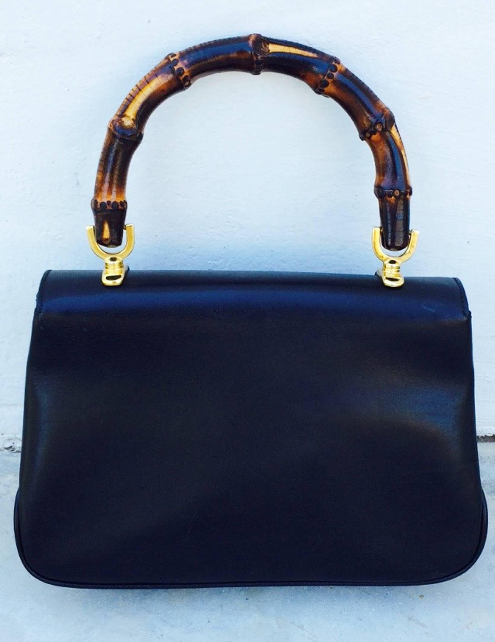A fine and now iconic bamboo handled Gucci handbag. Authentic sculpted black leather item features a vivid red leather interior with signature zipper pull. Two-tone silver/gold locking closure intact and working properly. Handle includes a 4