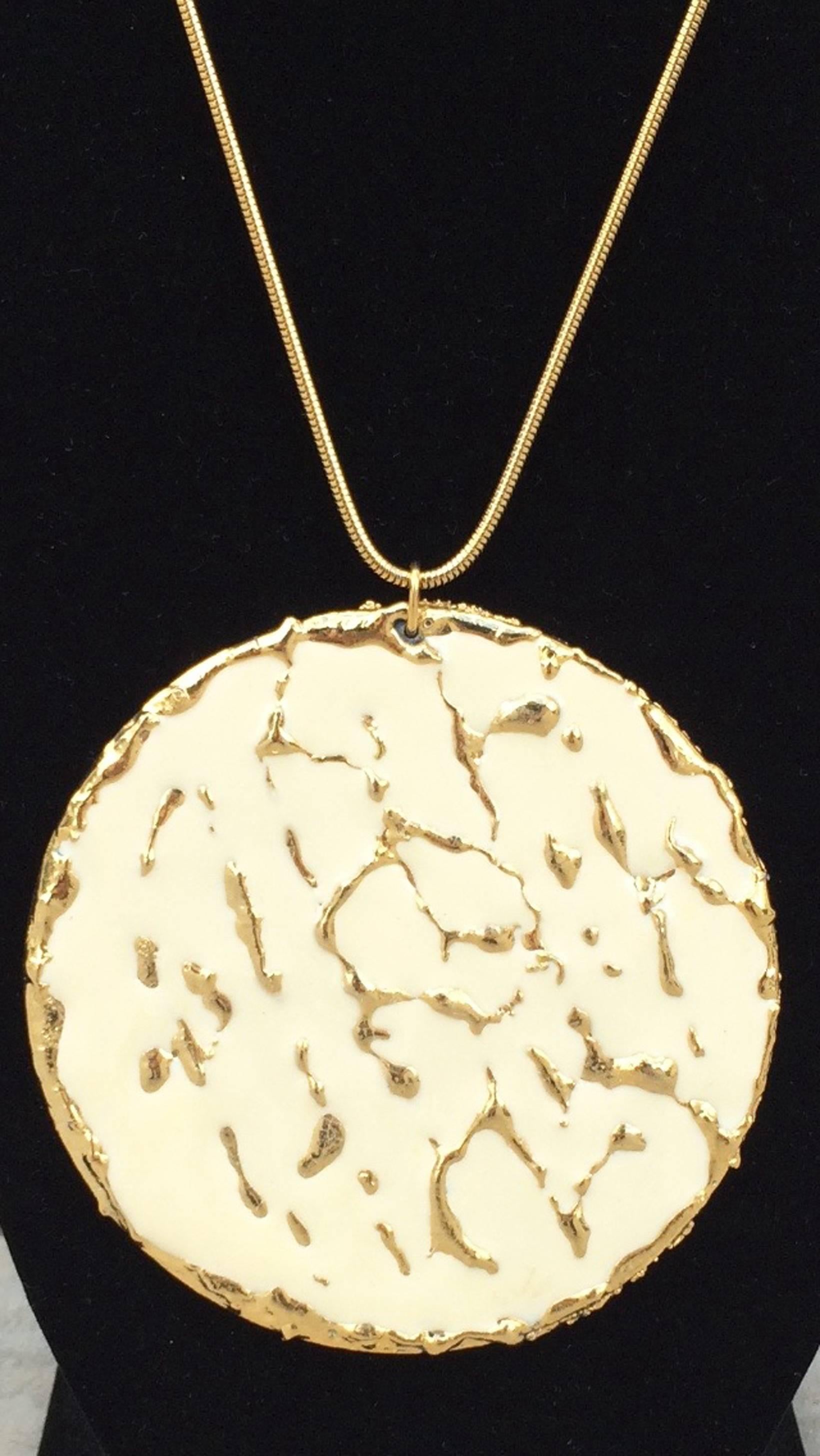 A fine and rare William de Lillo one-off prototype pendant necklace. Hand constructed gilt metal item features a cream enamel front in the brutalist manner. Item suspends from a matching gilt snake chain with locking barrel closure. Item directly