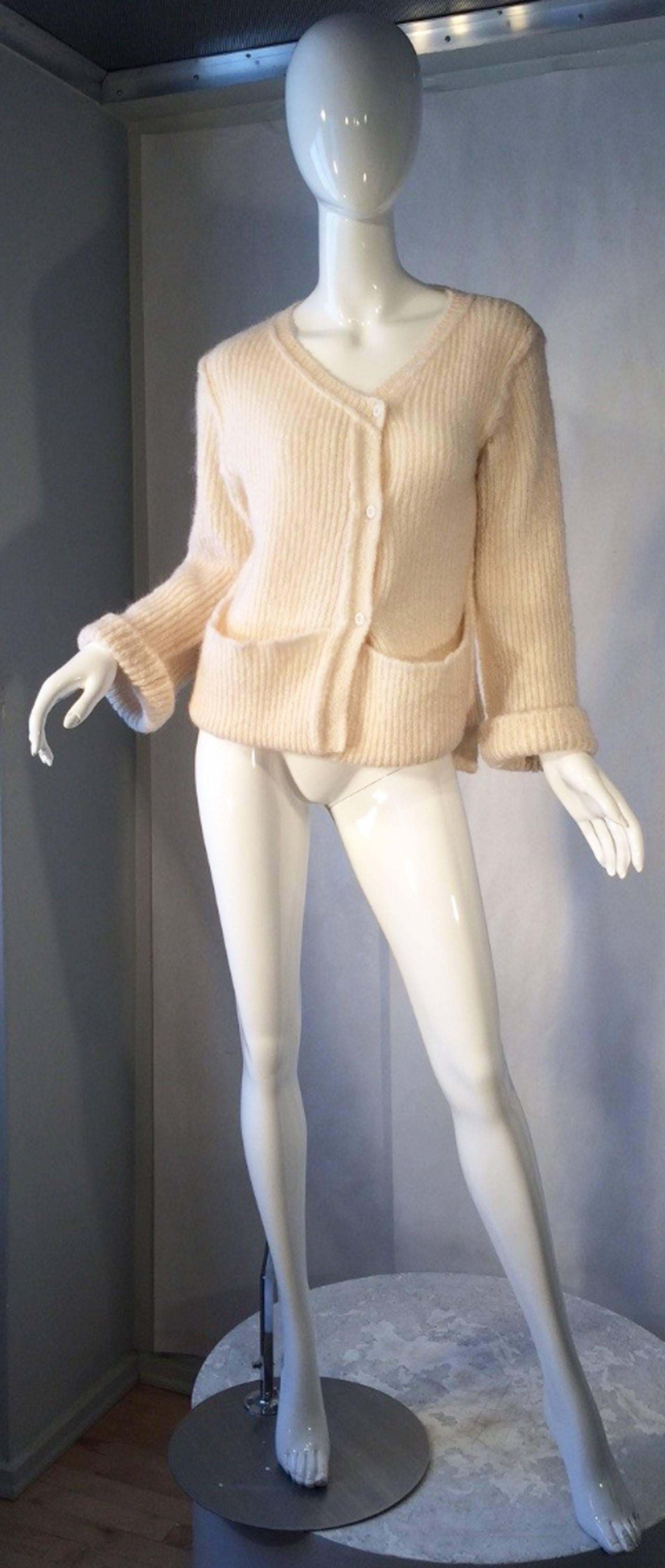 A fine and rare vintage Sonia Rykiel cardigan sweater. Early example of the designers now iconic knit designs features a asymmetrical hemline, open front pockets, turn-up cuffs and button front closures. Ivory cable knit wool item made in Italy for