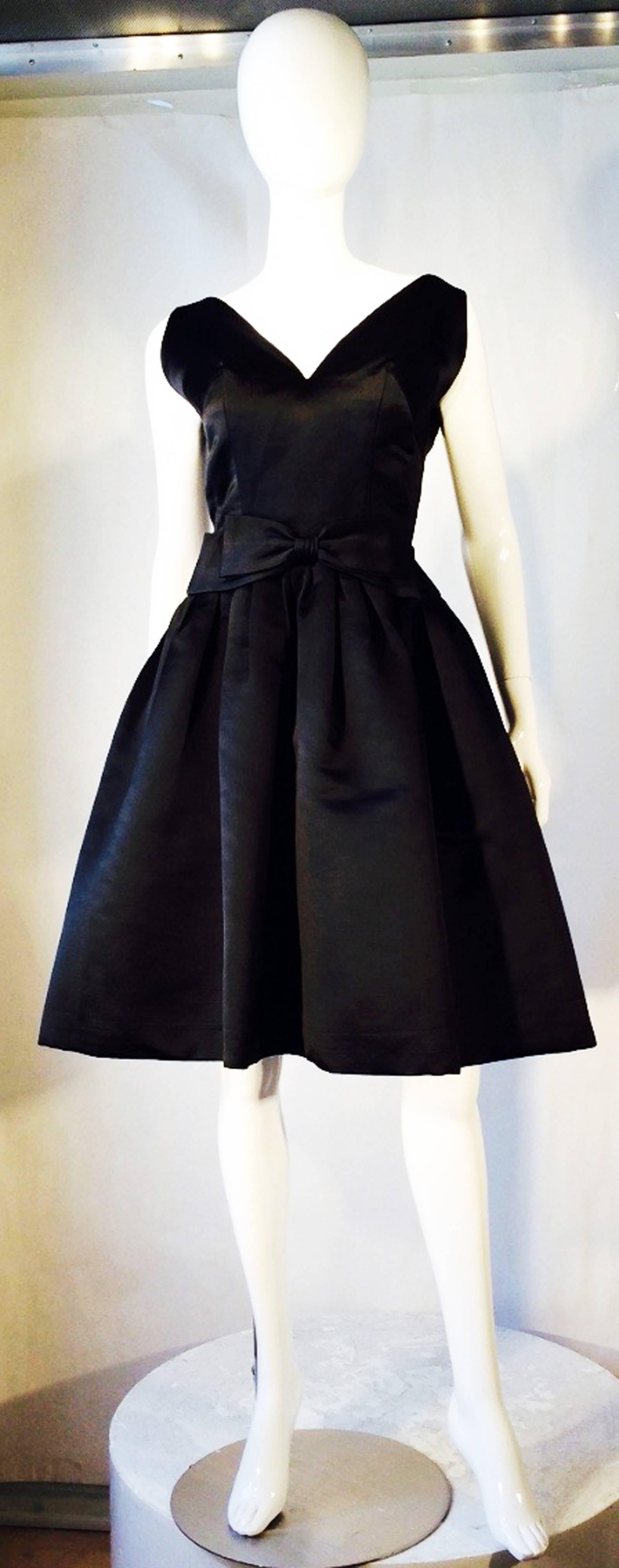 A fine and rare vintage Helga little black cocktail dress. Authentic couture ordered item thru Marshall Field 28 Shop ca.1960. Fine jet black silk satin taffeta fabric item features a boned bodice, nipped waist and fulled stiffened silk skirt. Item