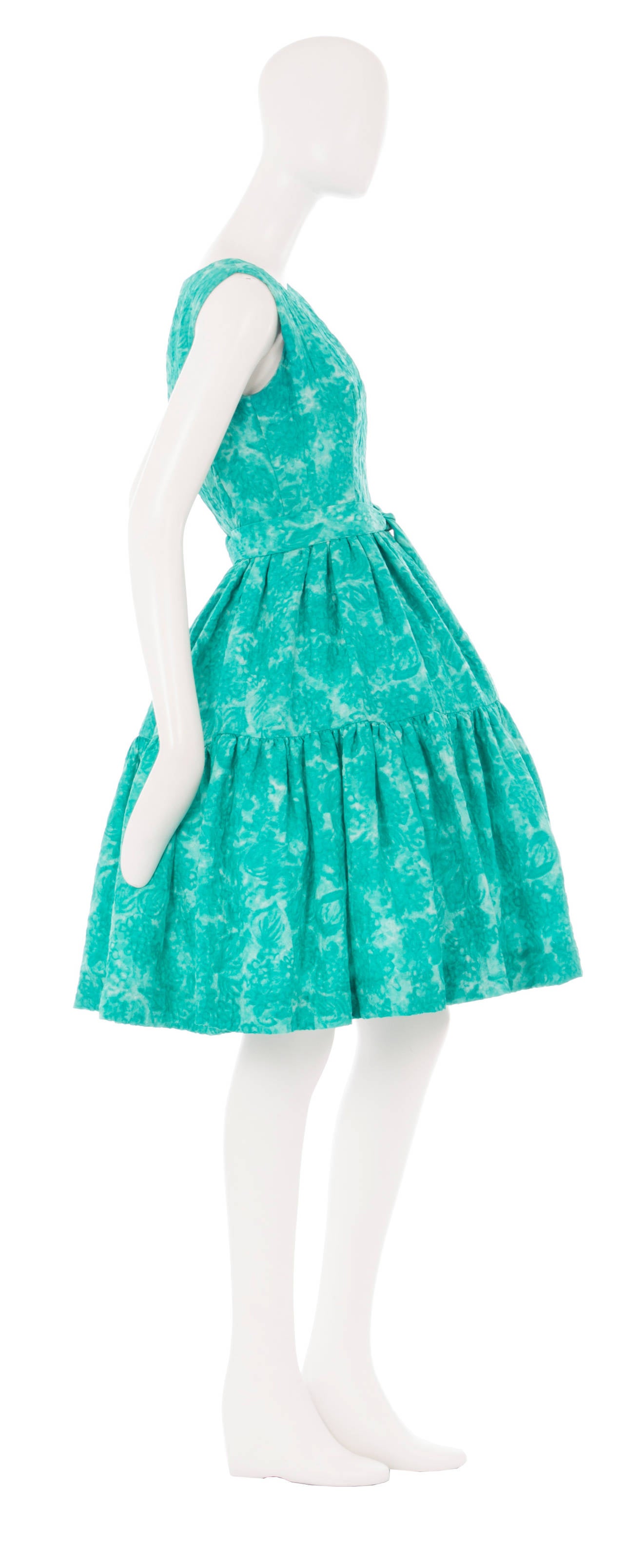 This incredibly chic haute couture day dress by Balenciaga is the ideal choice for a summer event. Constructed from turquoise green silk with a watercolour floral motif within the fabric, the dress features a fabric-matched belt at the waist and is