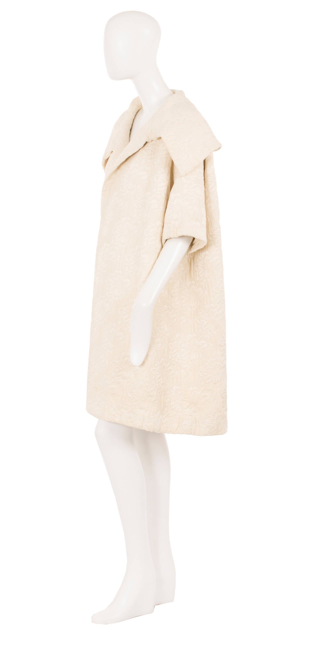 A fantastic example of Balenciaga’s signature style, this swing coat has the most incredible silhouette. Constructed in sumptuous ivory cotton matelasse, with a floral motif, the coat has no fastenings and elbow length sleeves. An exaggerated shawl