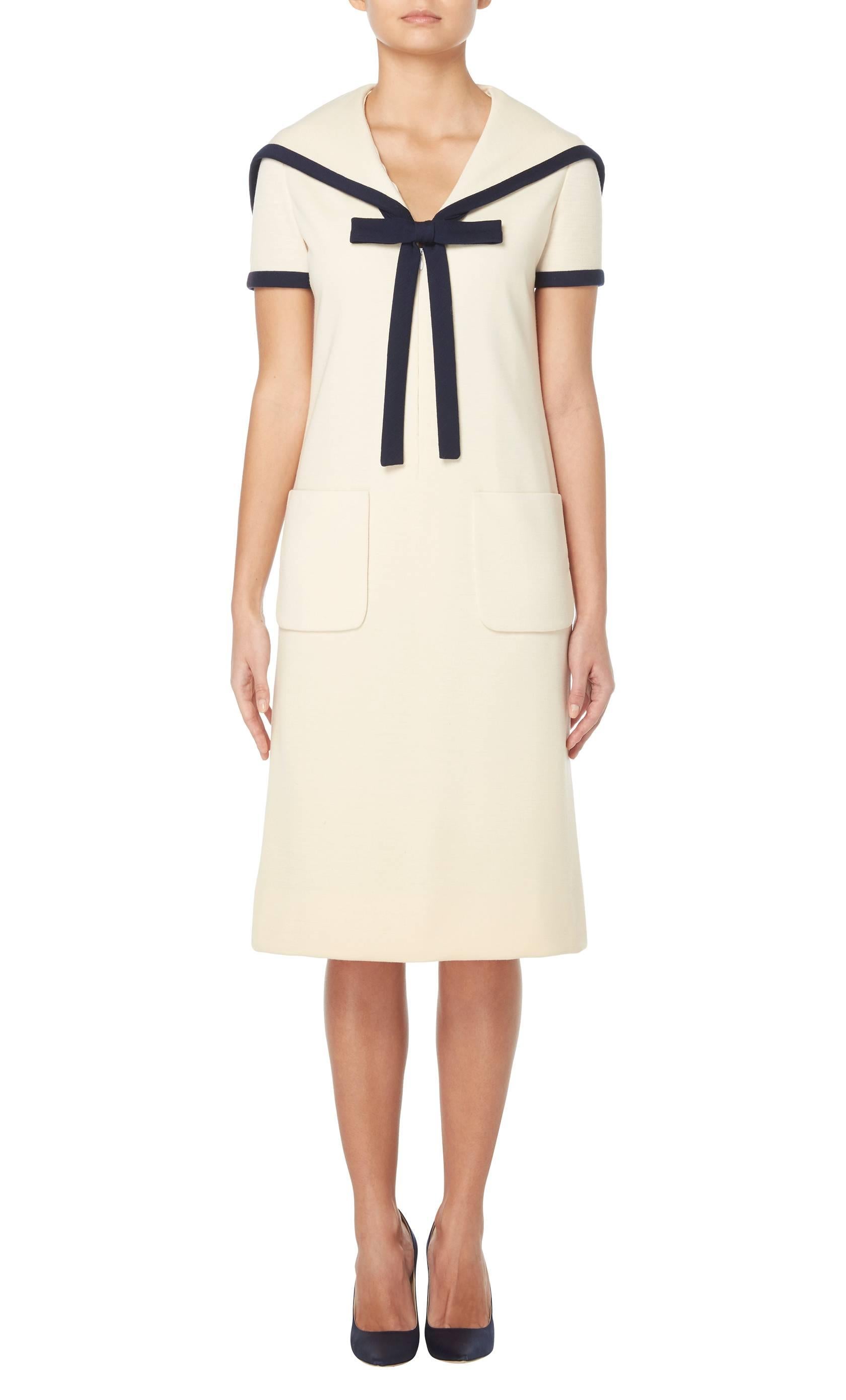 A fun, nautical-inspired piece, this dress by Bill Blass is great for daytime occasions. Constructed in ivory wool and featuring navy trim to the sailor collar and short sleeves, the dress has a bow detail on the neckline and stars embroidered at