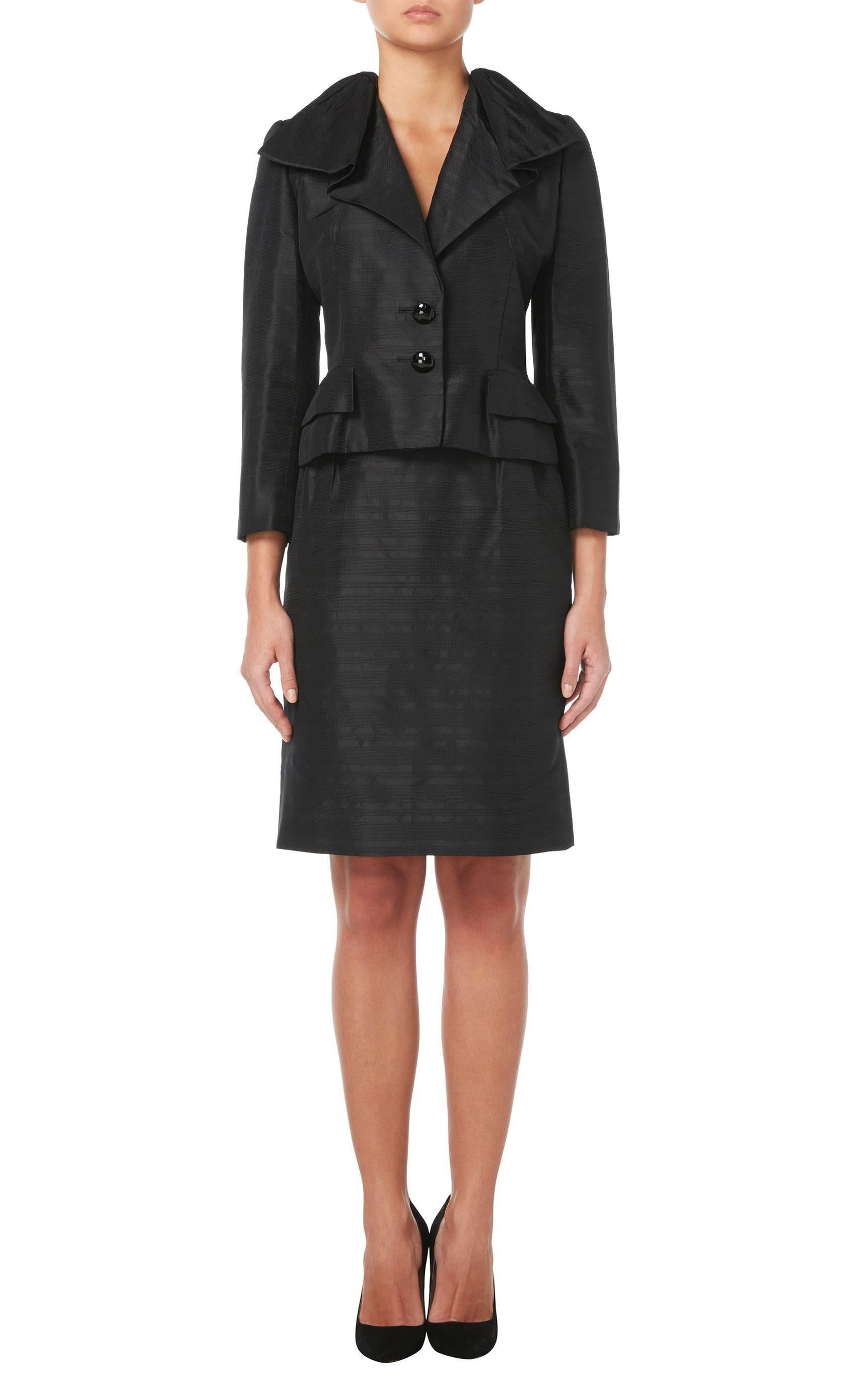 Whether for the office or an evening event, this Dior haute couture suit will look fabulous. Comprised of a jacket and in skirt in matching black silk, the jacket features a dramatic ruffle collar. Black faceted buttons to the front and cuffs of add