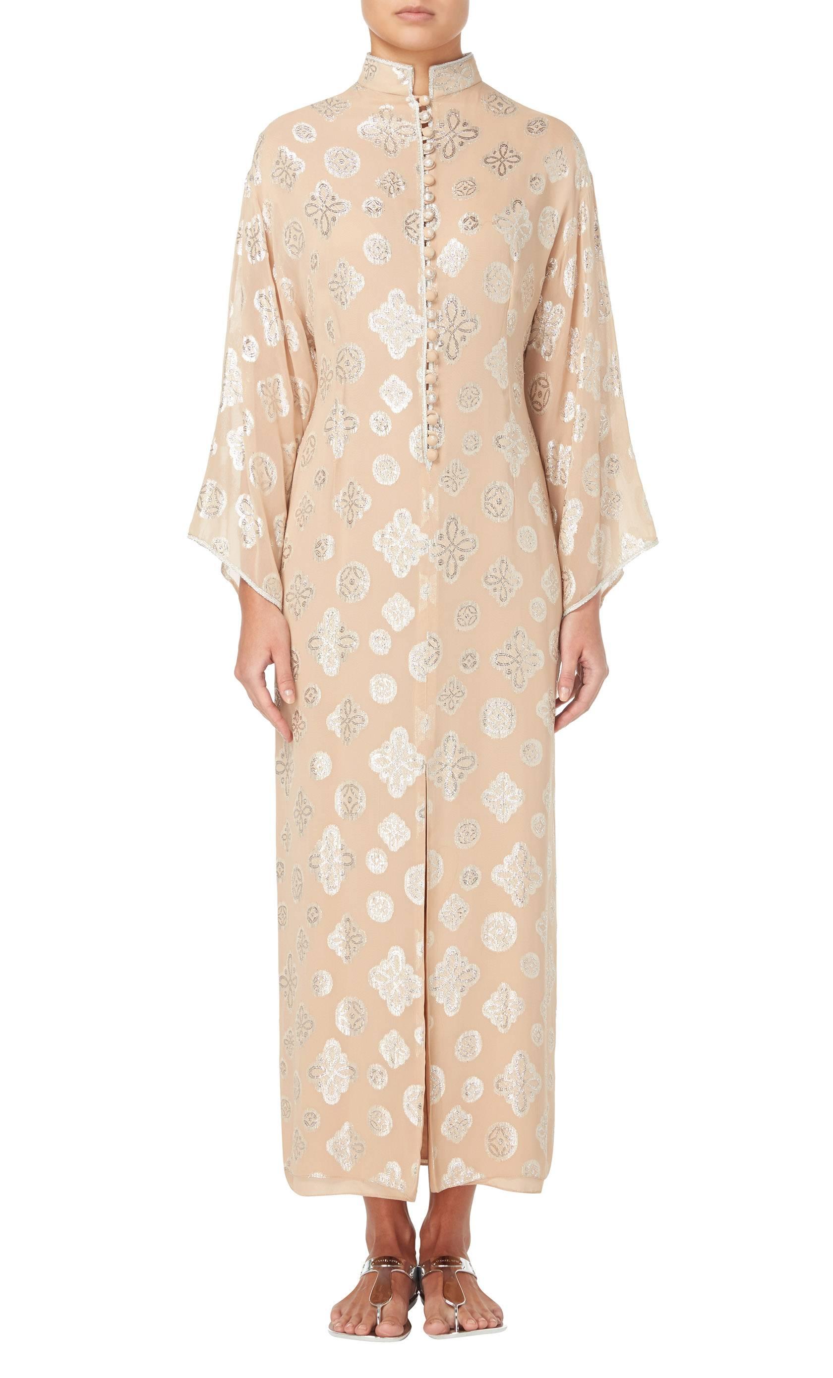 This Oscar de la Renta dress has a relaxed, bohemian feel, perfect for holidays and hot summer nights. Constructed in apricot synthetic chiffon with a silver Lurex paisley pattern, the dress features a high neckline and twenty fabric covered buttons