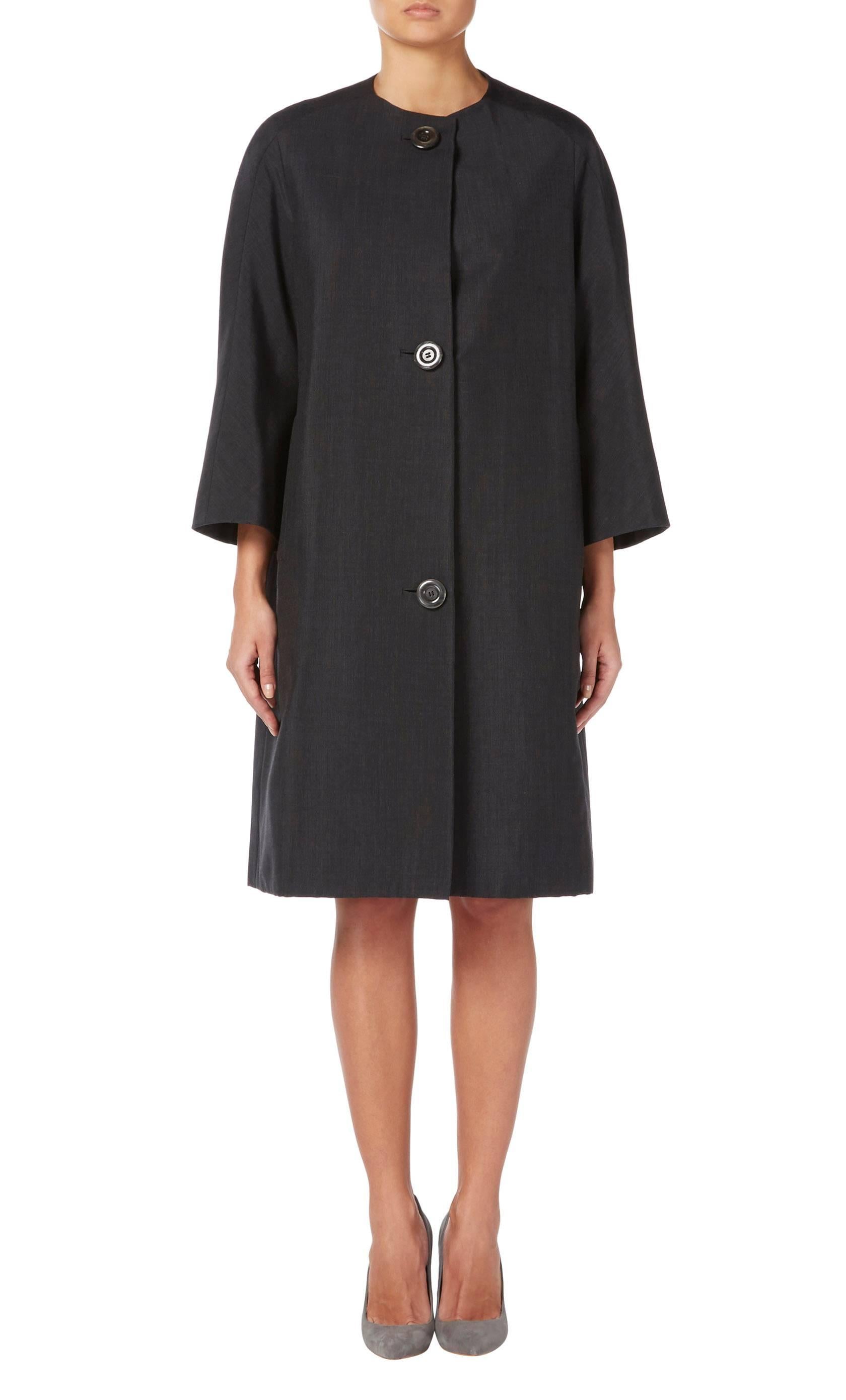 With a classic 60s swing cut, this flattering Dior haute couture coat is a fantastic piece for layering. Constructed in charcoal grey wool, the coat has a collarless neckline and slip pockets on the hip with three large buttons fastening to the