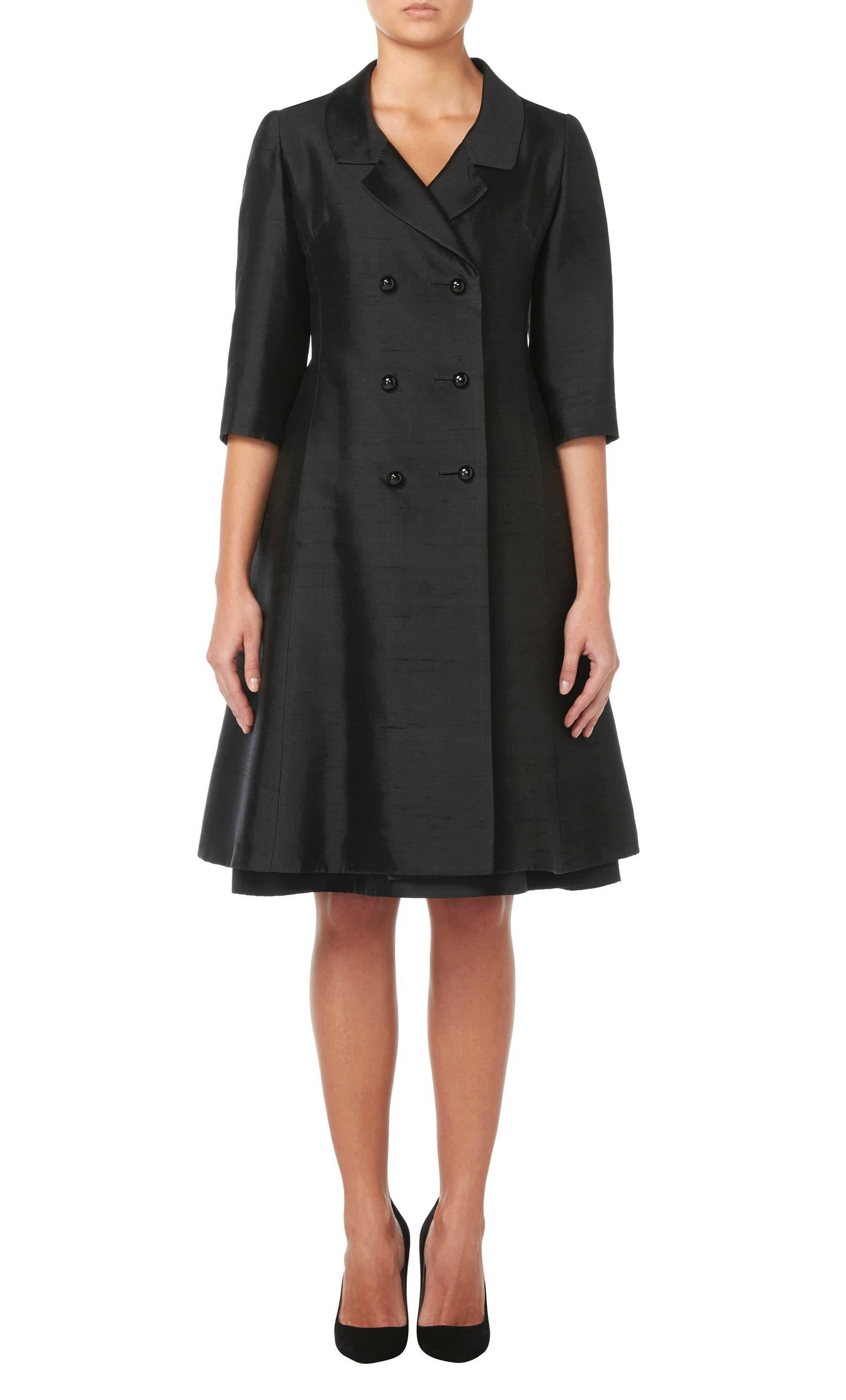 This incredibly chic Nina Ricci dress suit is constructed in black silk and is made up of a cocktail dress and double-breasted swing coat. The dress is tight fitting over the body, flaring into a full skirt and features bows at the shoulder for a