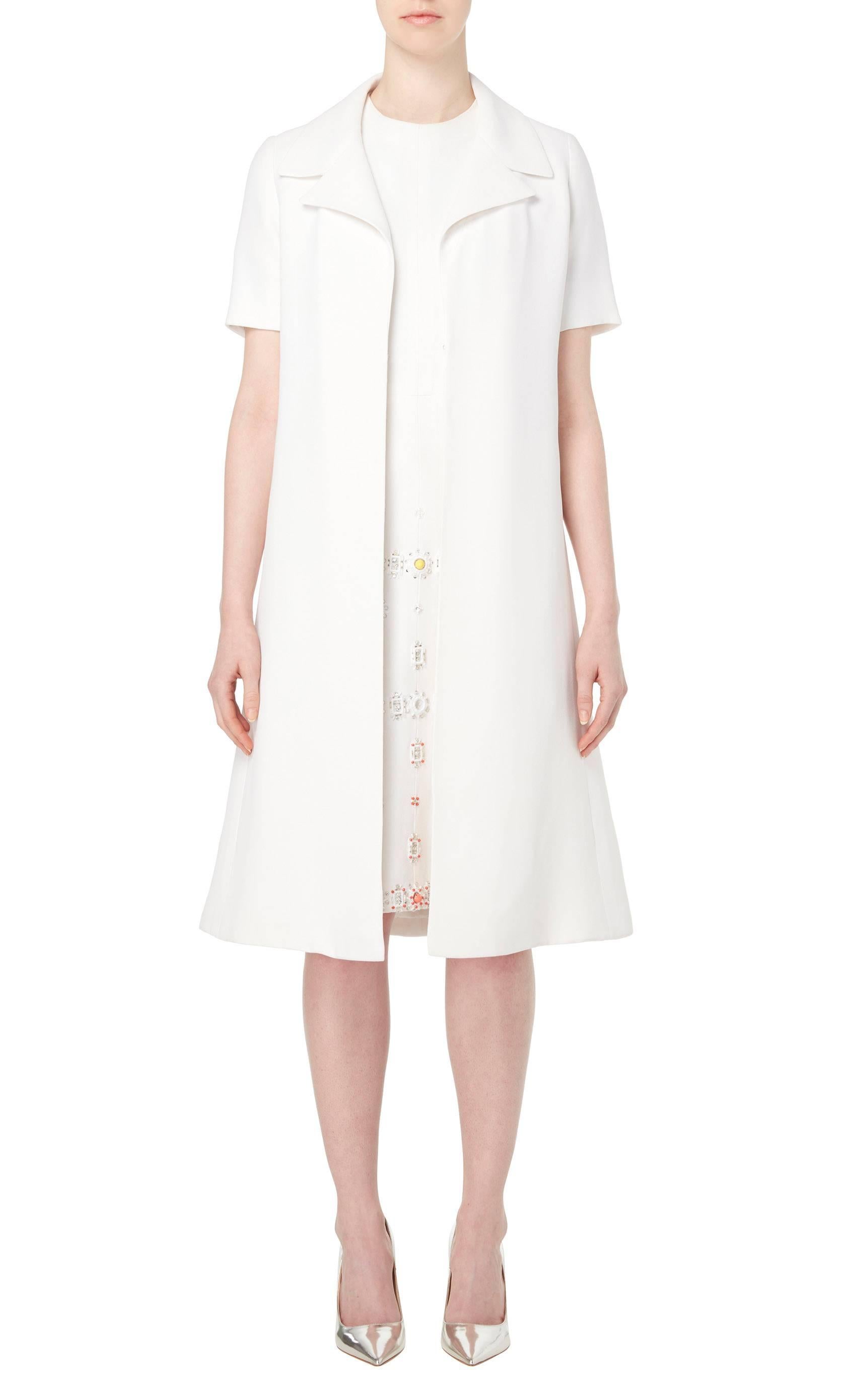 This Jean Patou two-piece consists of a dress and jacket, both in constructed ivory crepe. The dress features a round neckline, short sleeves and an A-line silhouette, while the skirt is embellished with rows of yellow, turquoise and coral domed