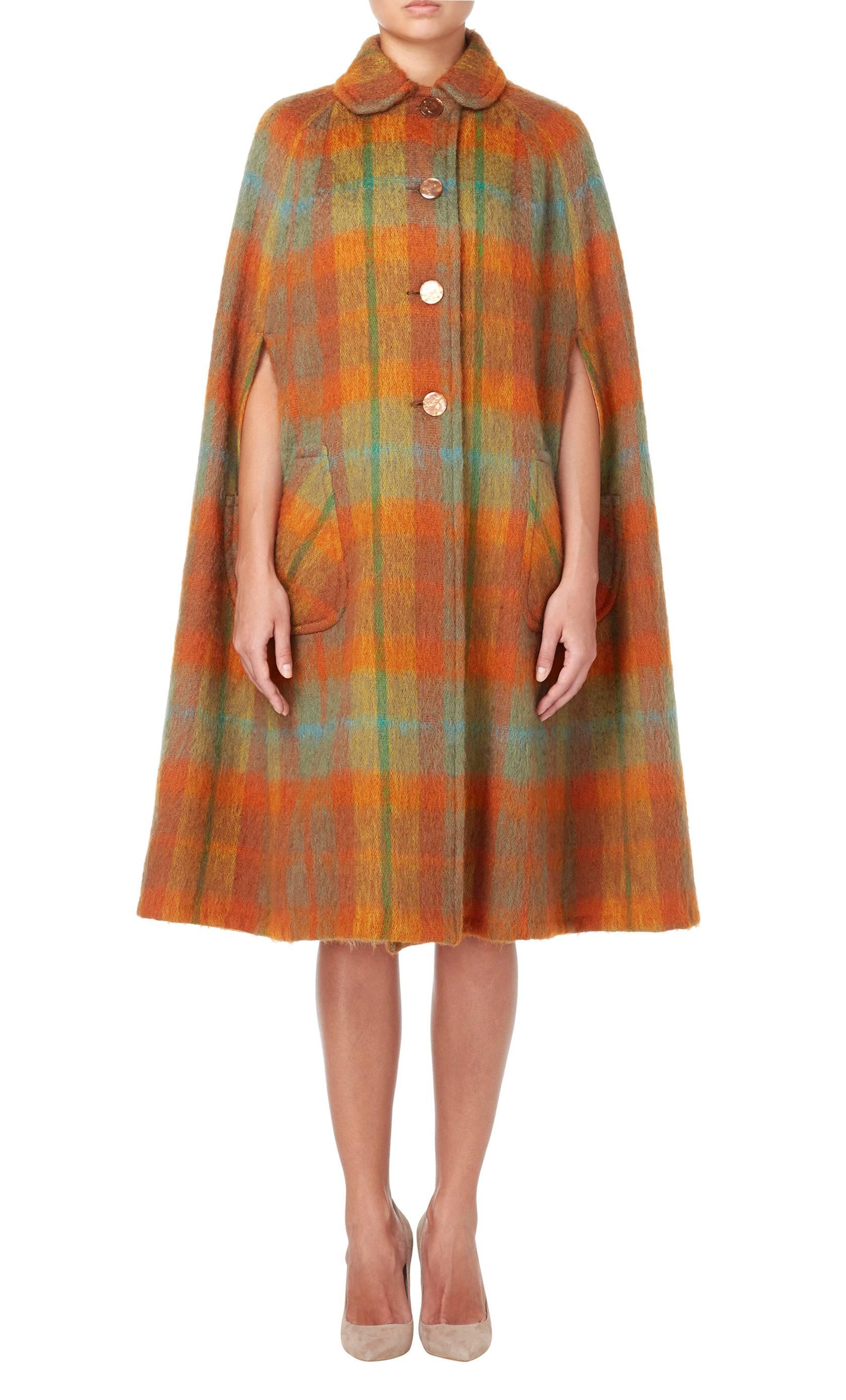 The autumnal hues of this 1970s Strathtay cape make this perfect for cold days and weekends in the country. Constructed in orange, brown and green checked mohair, the cape fastens with buttons to the front and features a peter pan collar and