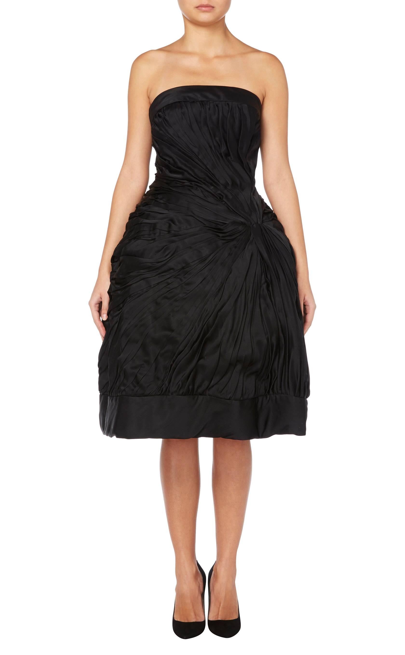 This fabulous strapless dress by Helena Barbieri, constructed in black silk, creates an amazing silhouette with a nipped in waist and exaggerated tulip style skirt. Boning in the waist gives additional support while the silk is ruched out from a