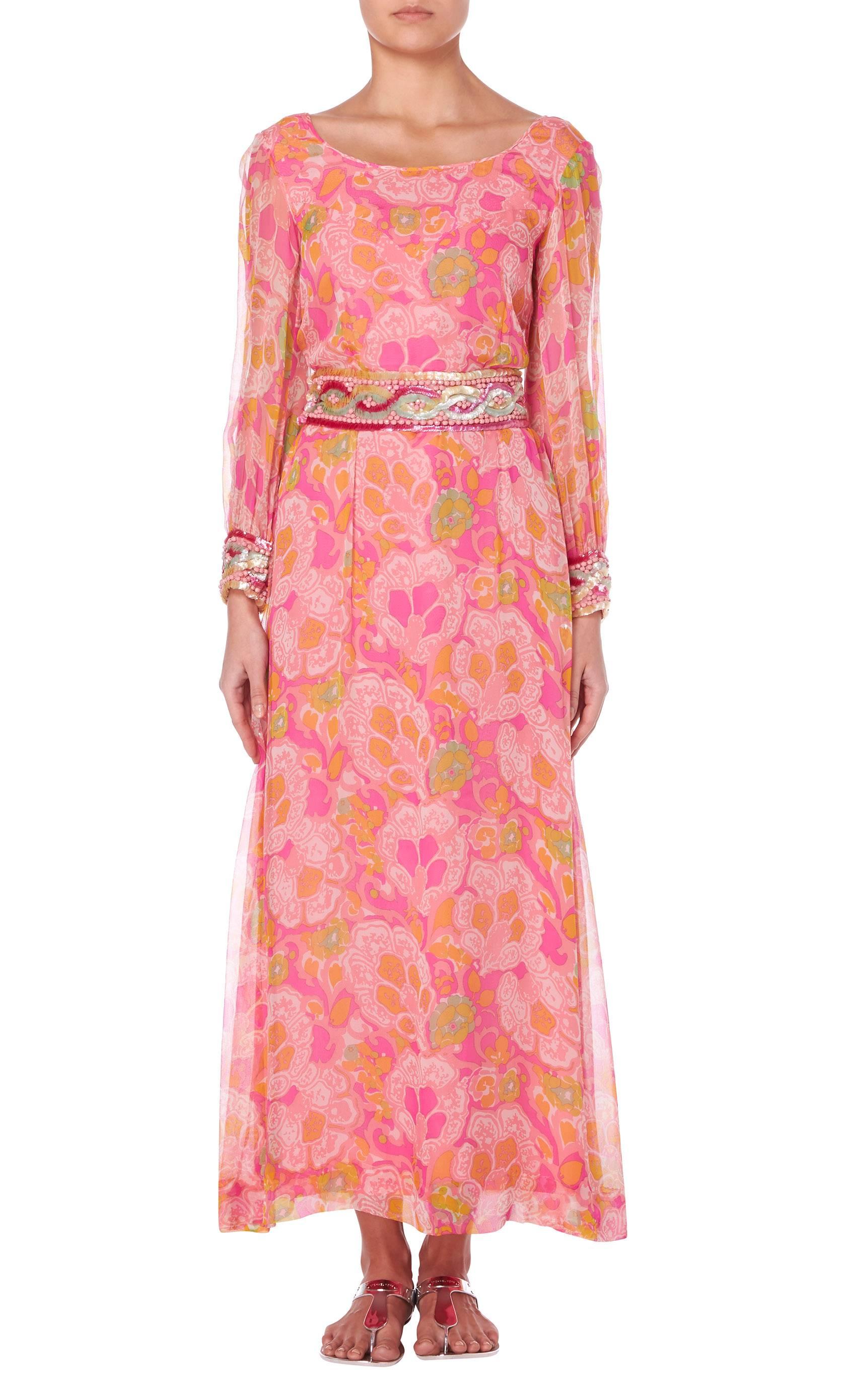 A bright and colourful maxi dress by Hardy Amies, constructed from silk chiffon in an orange, pink and green psychedelic print. The waistband is embellished with sequins and beads, drawing out the contrasting colours of the print. The dress is fully