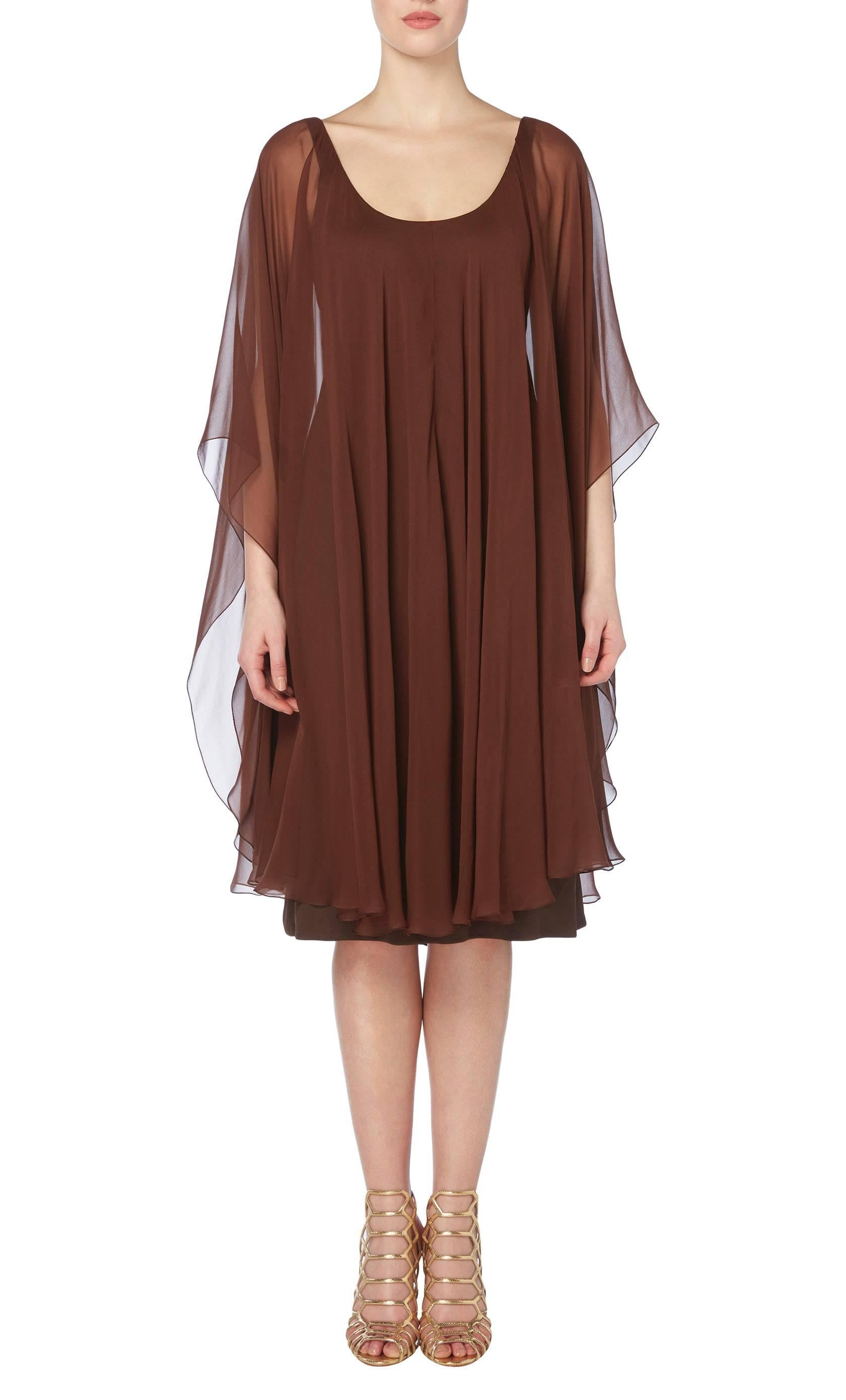 Subtly sexy, this Halston cocktail dress will look fabulous teamed with gold accessories. With a close fitting brown jersey underdress, the dress features an integral cape of sheer chiffon falls over the body creating movement, making this the