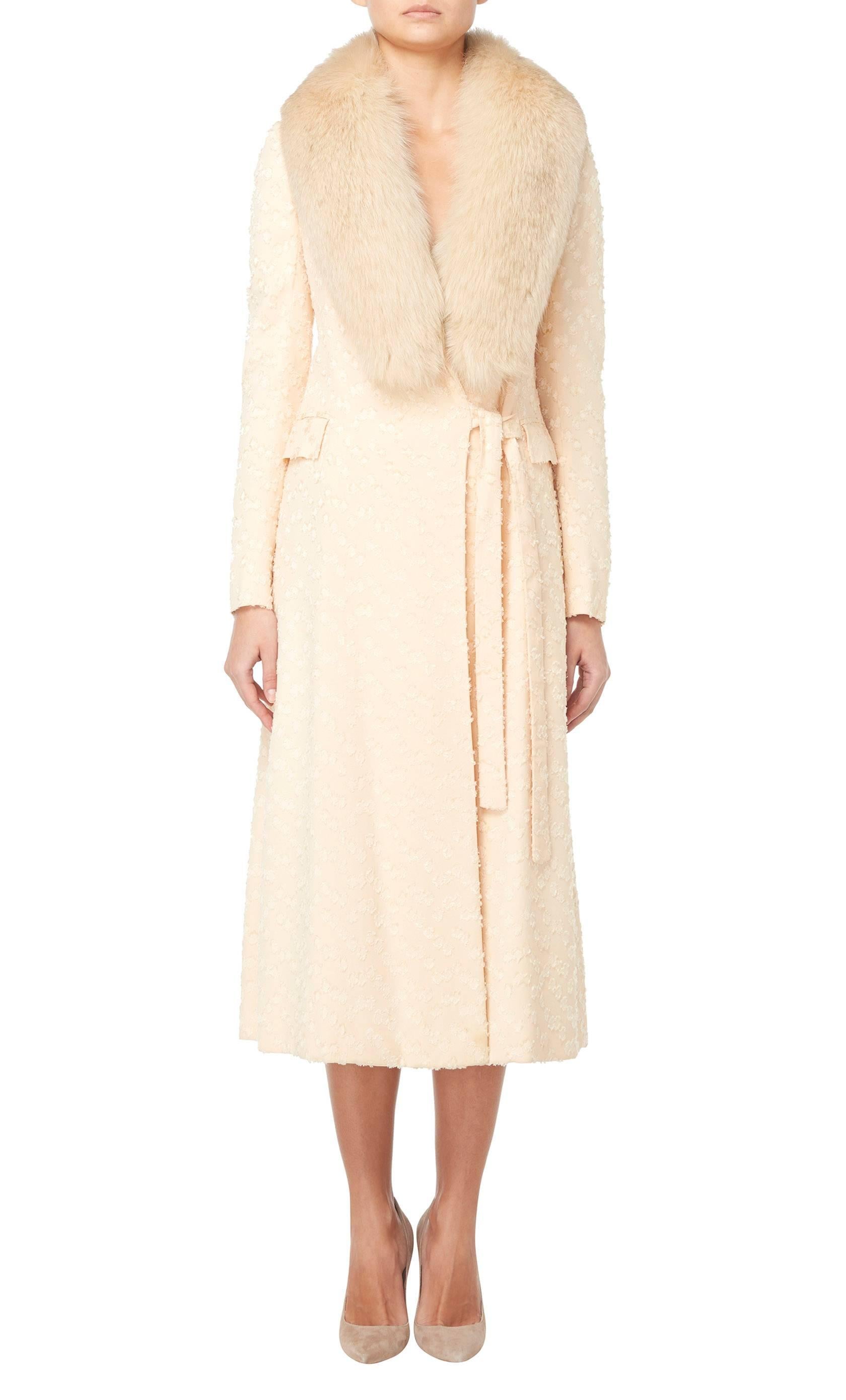 Constructed in apricot clip dot silk, this Adolfo coat features an ivory fox fur collar. With a wrap over style, the coat ties on the waist, adding definition to the silhouette and features pockets on the hip.

Constructed in pale orange clip dot