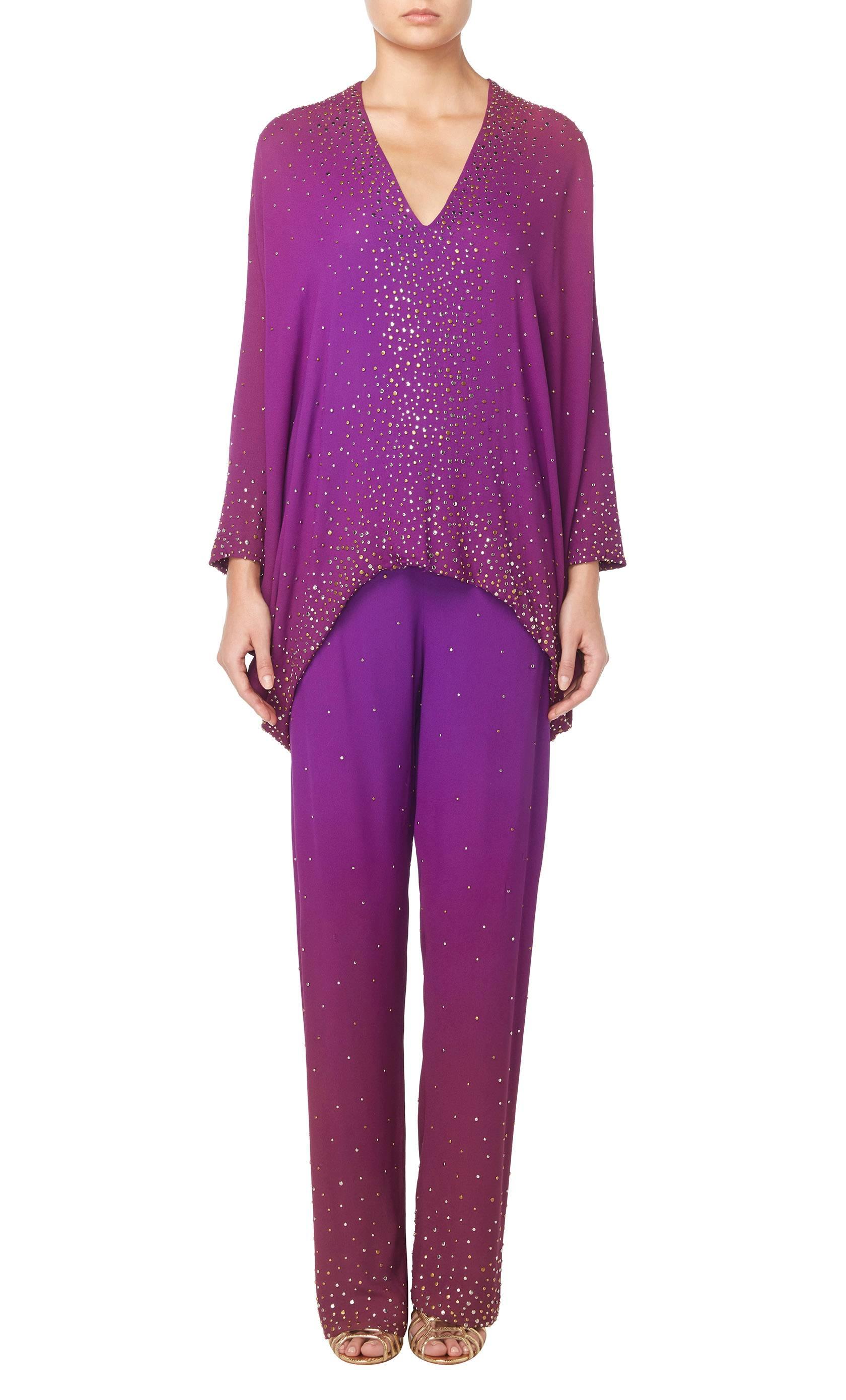 This amazing Halston ensemble is a colourful option for an evening event. Constructed from ombre purple silk, the suit is made up of an oversized top and wide leg trousers embellished with gold and silver studwork, adding a touch of sparkle. The top