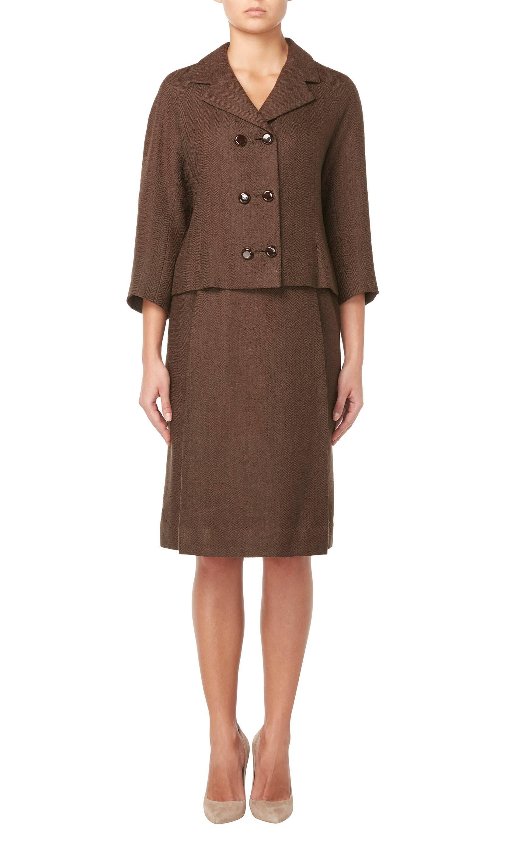 A beautifully tailored haute couture suit by Balenciaga himself. Constructed in fine brown wool with a herringbone weave, the double-breasted jacket has its original brown lacquer and gilt buttons, while the skirt features two hidden pockets and