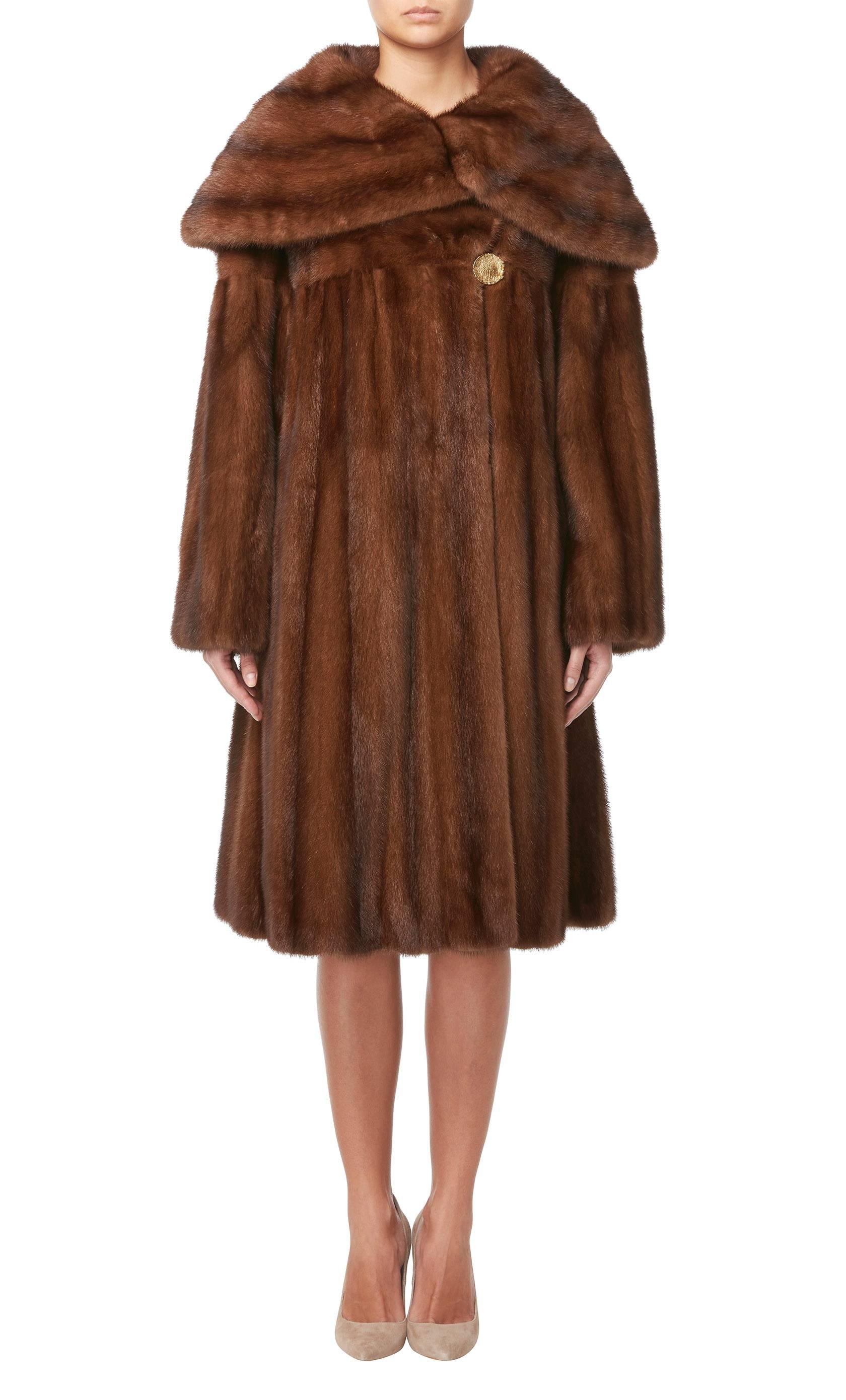 This Marie Martine coat is constructed in soft brown mink fur and is perfect for cold winter days or nights. With a wide caped collar, the coat fastens with a single god metal button to the front and has inside pockets on the hip.

Constructed in