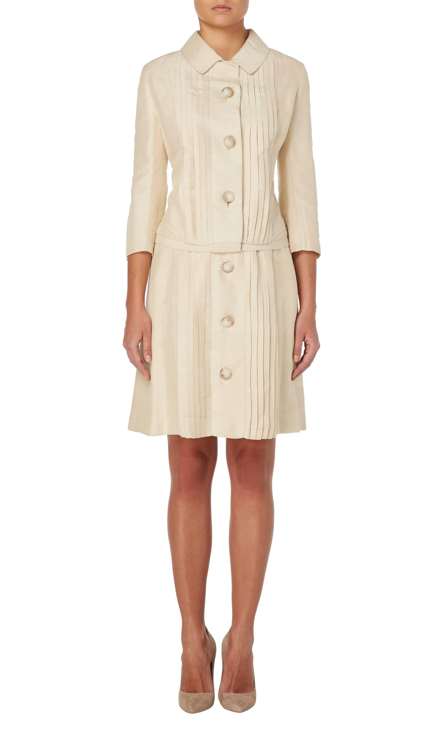 Constructed in fine pale beige silk, this lightweight and pleated skirt suit by Jean Patou is will make for a refreshing summer look. Lined in ivory silk and with the original pale horn buttons, the suit is designed to be less structured and is more